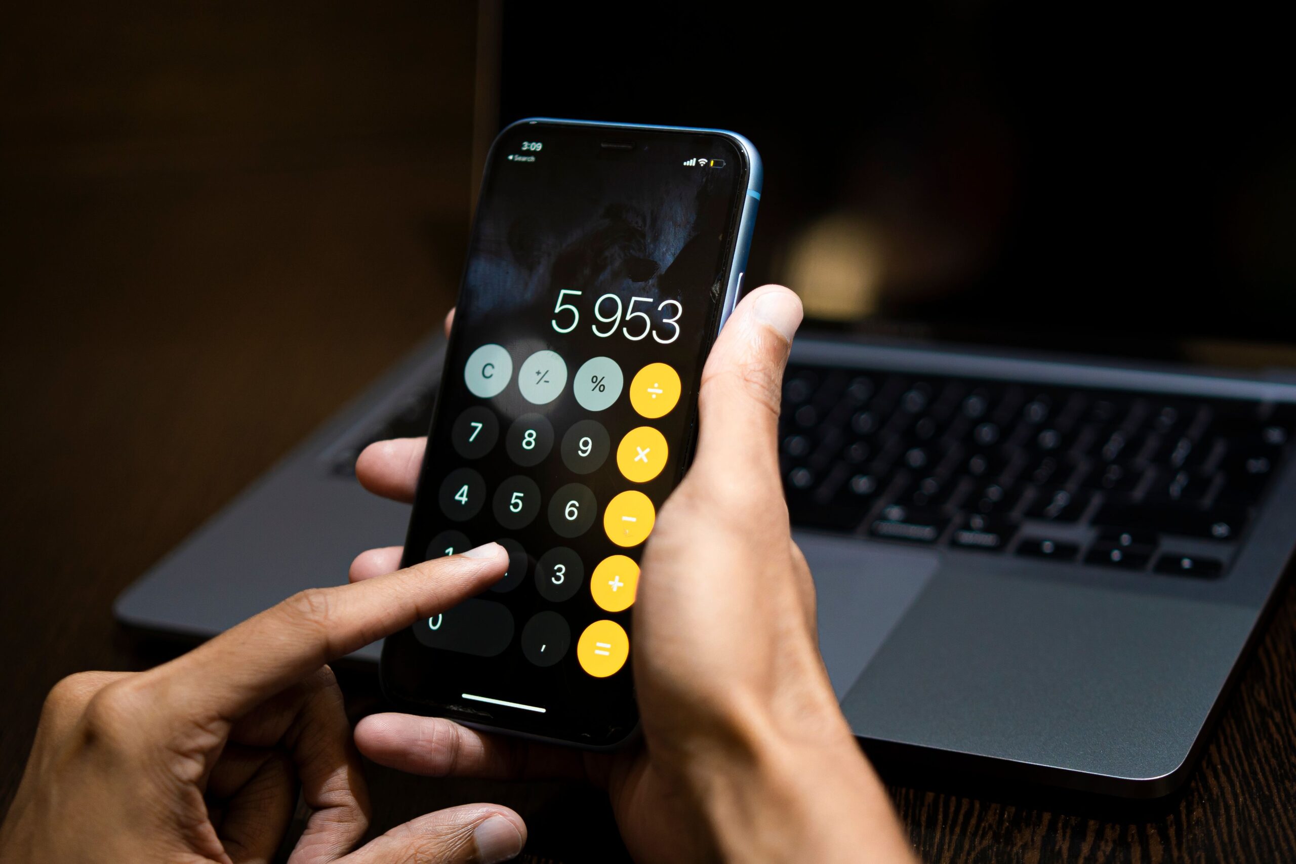 Uso de aplicación de calculadora en smartphone con una laptop al fondo, simbolizando la digitalización de los procesos contables y administrativos.