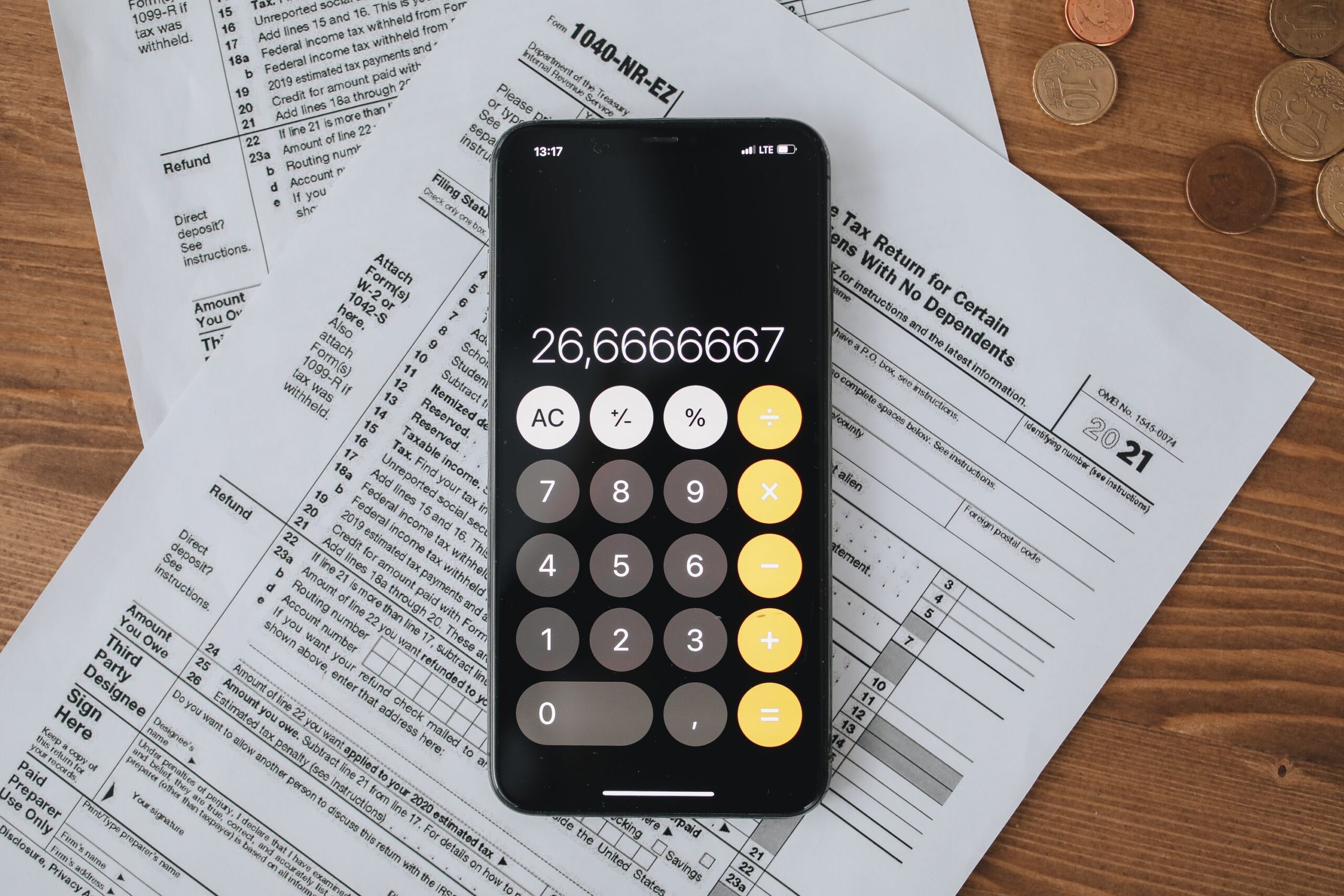 Teléfono inteligente con aplicación de calculadora sobre formularios de impuestos oficiales y monedas, ilustrando la preparación fiscal y el cálculo de IVA.
