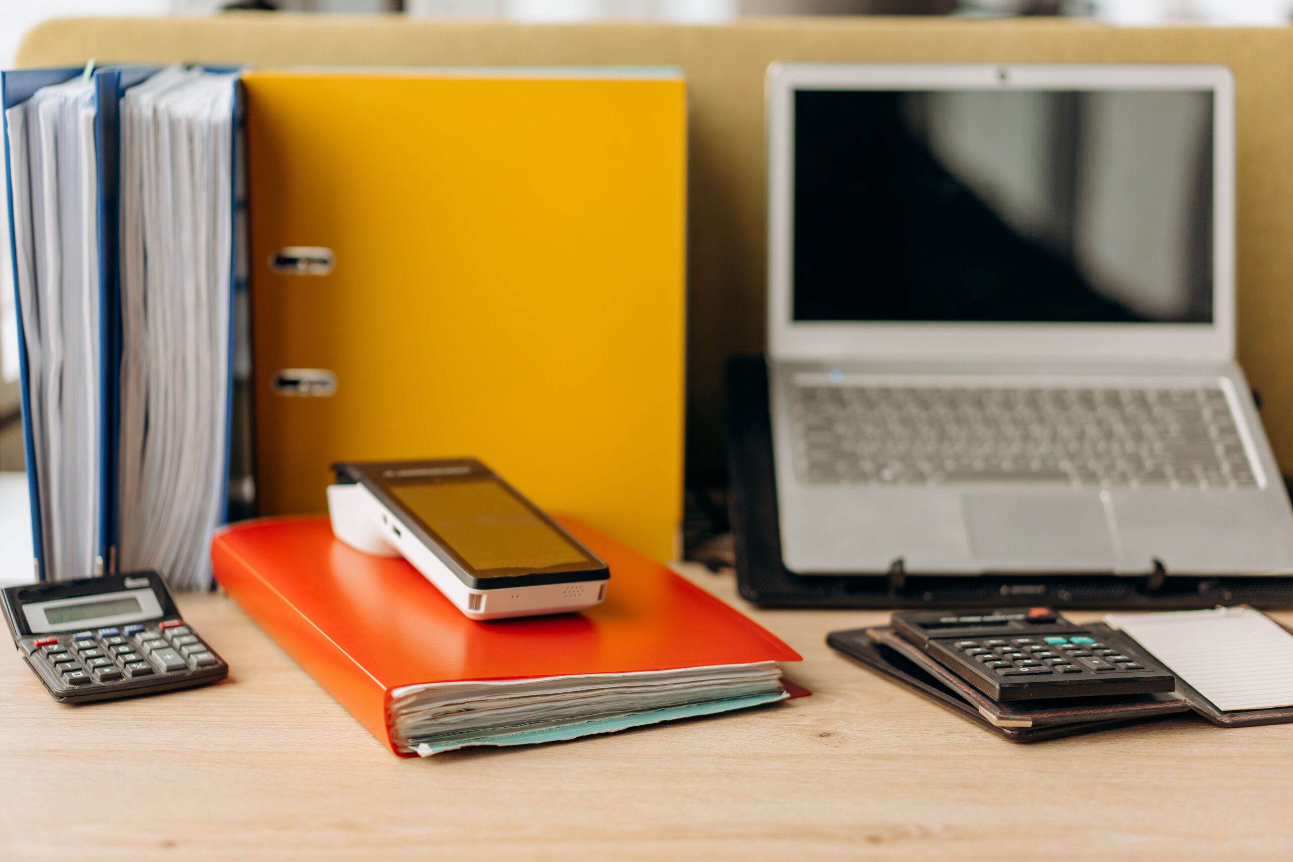 Escritorio de oficina moderno y organizado con laptop, smartphone, calculadoras y carpetas de documentos, ideal para representar la productividad administrativa.