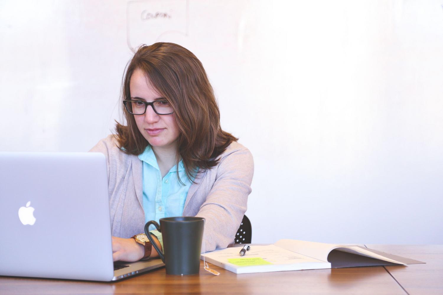 Mujer de negocios enfocada utilizando un portátil y una agenda para organizar sus tareas.