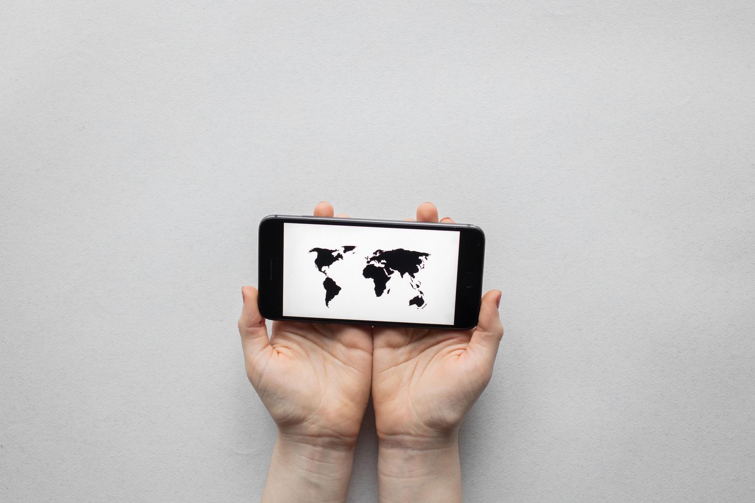Manos sosteniendo un smartphone que muestra un mapa mundial, simbolizando la expansión global de una tienda online.