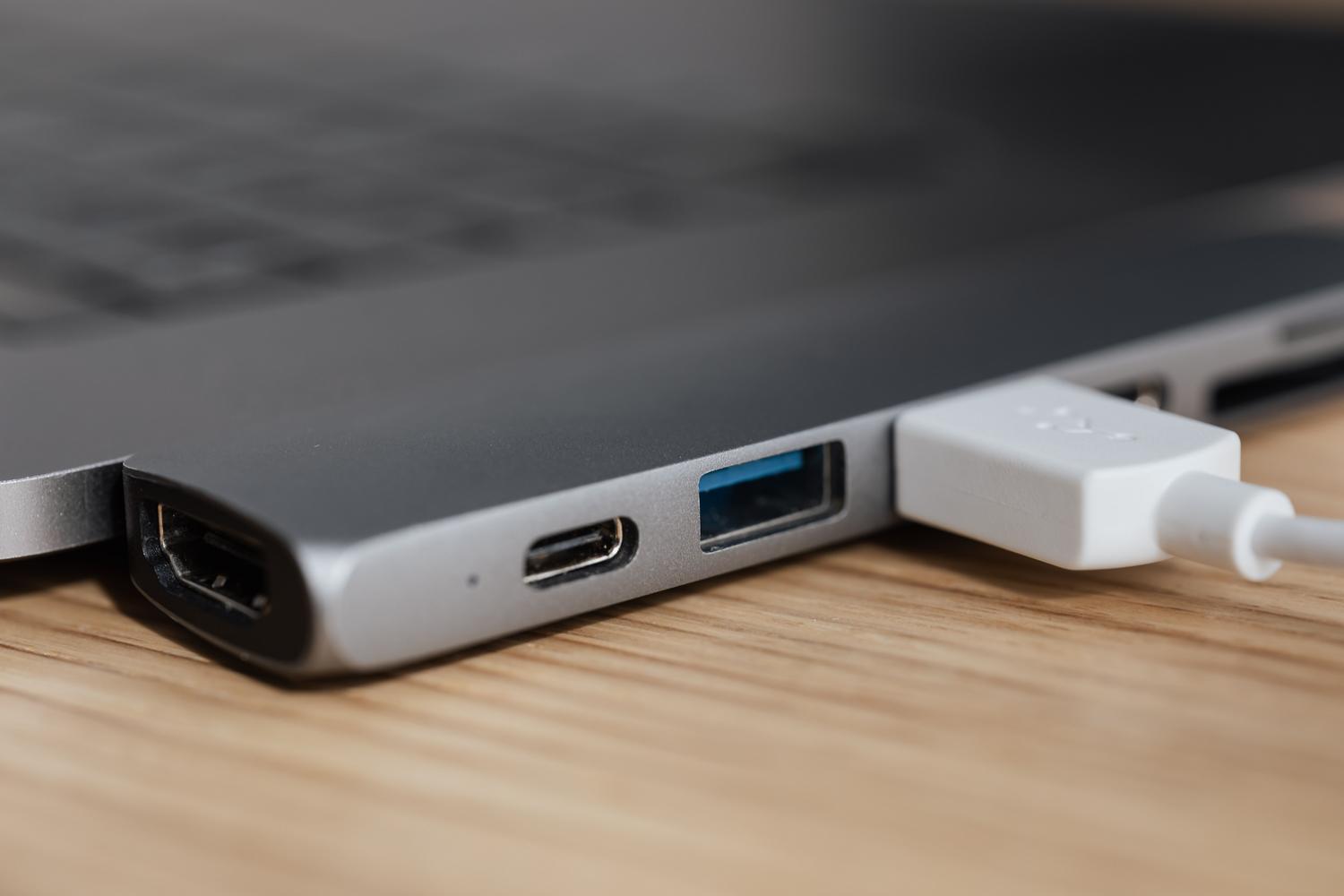 Adaptador multiport USB-C conectado a un ordenador portátil moderno sobre una mesa de madera.