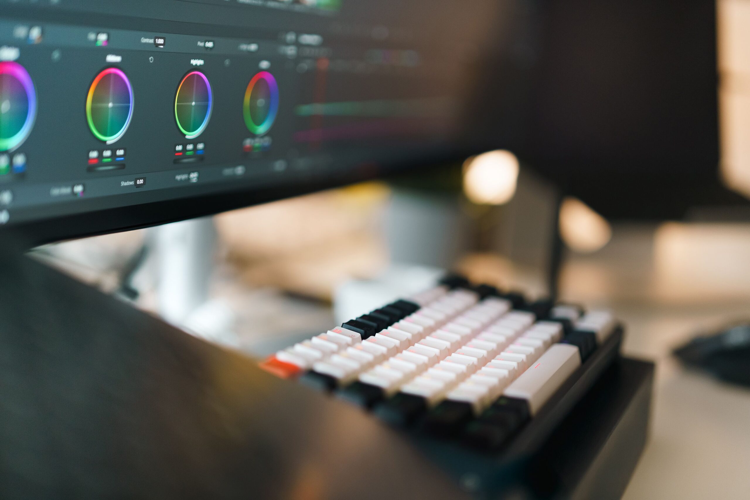Primer plano de un setup de edición de vídeo profesional con teclado mecánico y proceso de gradación de color en pantalla.