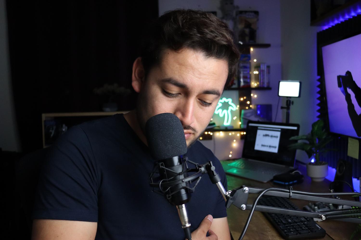 Persona grabando voz con un micrófono de condensador y brazo articulado en un rincón de producción casera. Persona grabando voz con un micrófono de condensador y brazo articulado en un rincón de producción casera.