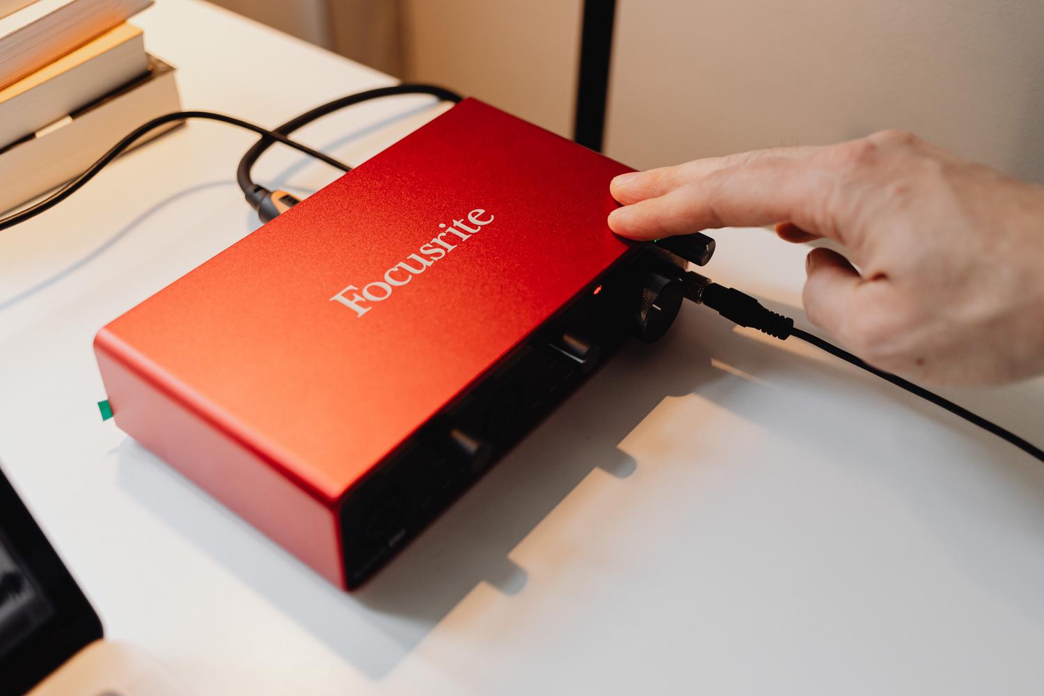 Primer plano de una interfaz de audio Focusrite roja siendo ajustada en un escritorio de estudio casero. Primer plano de una interfaz de audio Focusrite roja siendo ajustada en un escritorio de estudio casero.