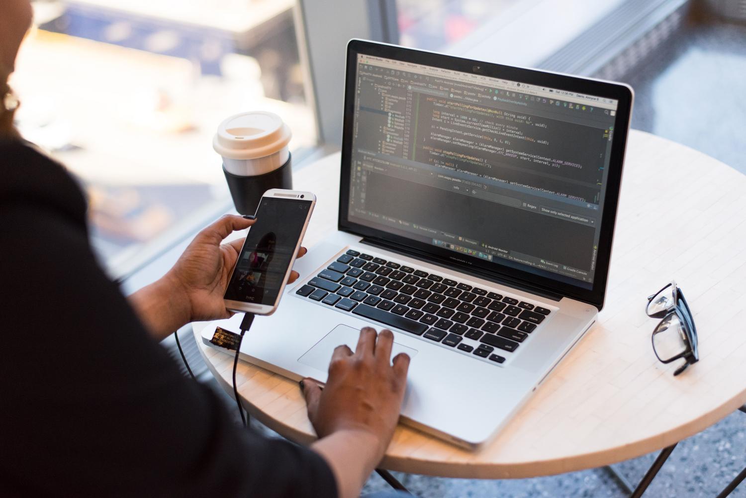 Desarrollador utilizando un portátil y un smartphone, representando la implementación de medidas de seguridad como la autenticación de dos pasos (2FA).