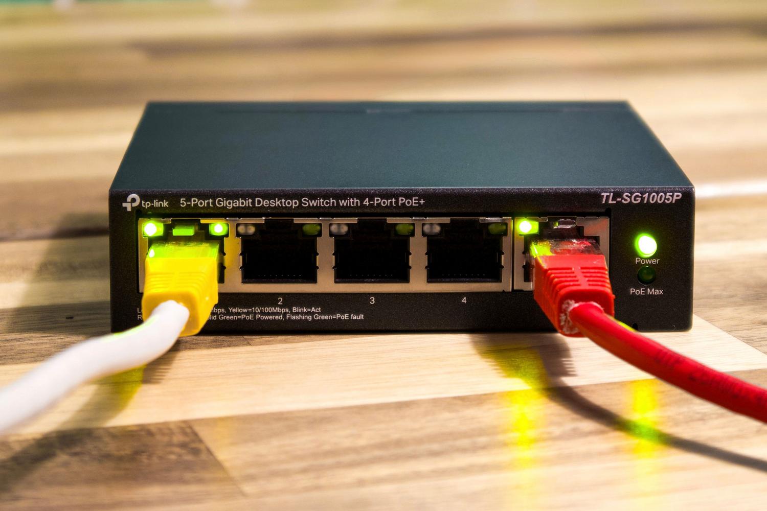Switch de red Ethernet con cables conectados sobre una superficie de madera, ilustrando la gestión de conexiones fijas.