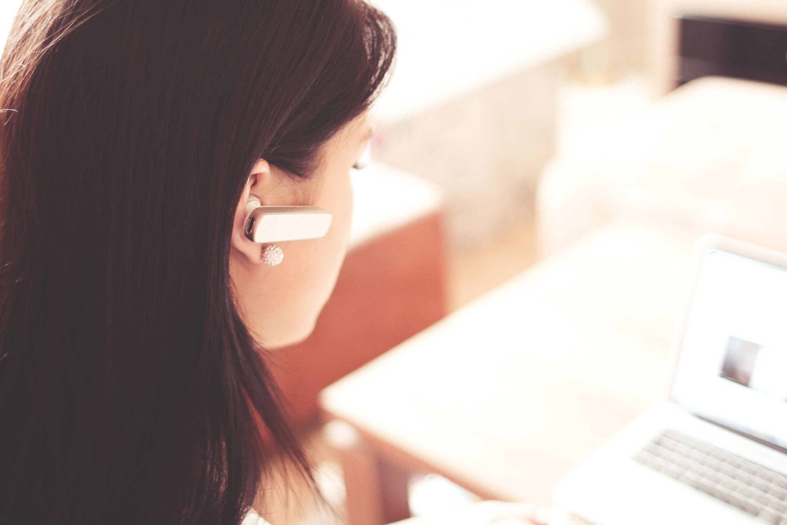 Profesional utilizando un auricular Bluetooth mientras trabaja con su computadora portátil