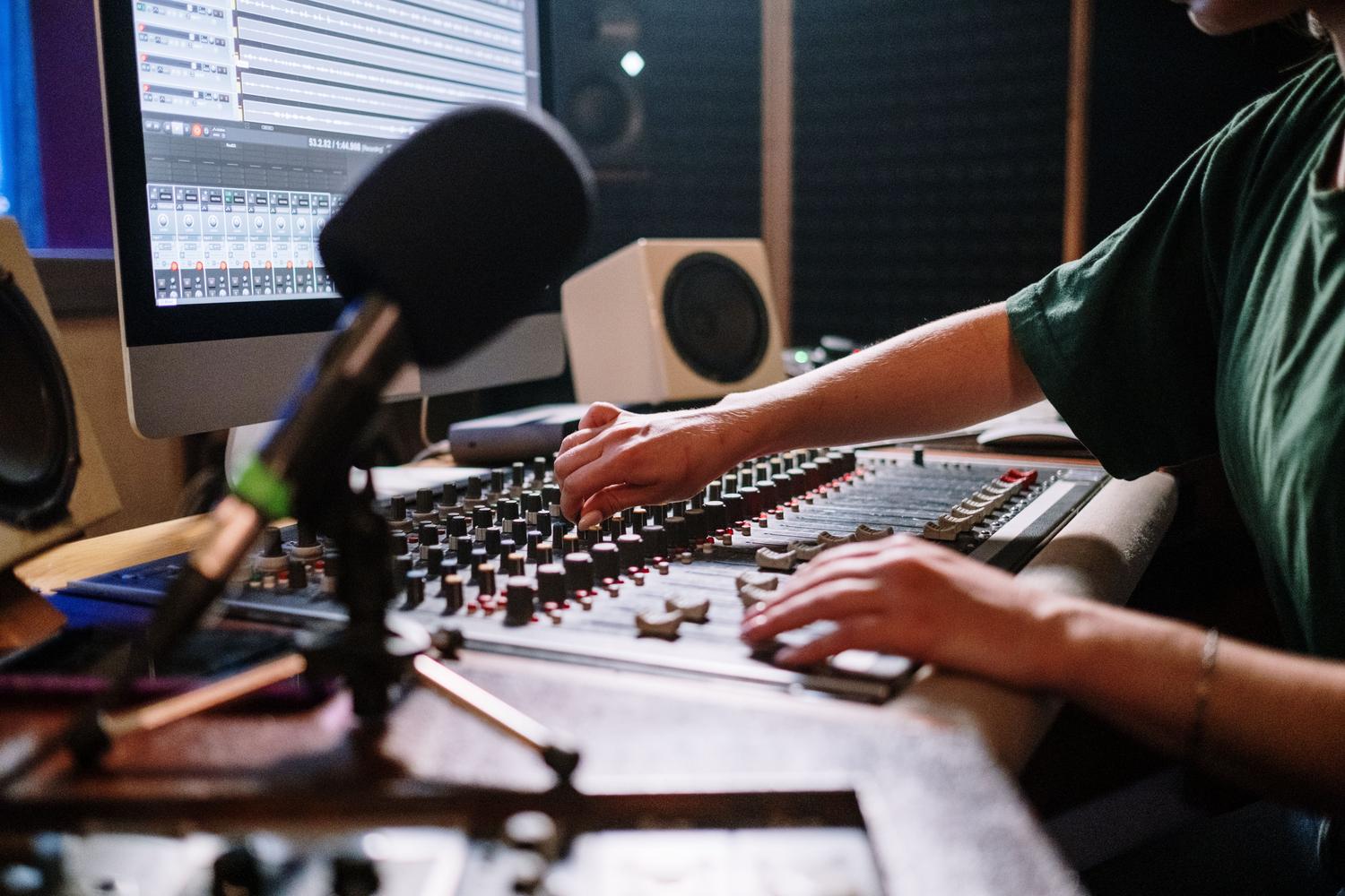 Ingeniero de sonido ajustando una consola de mezclas, ideal para representar la fase de mezcla donde se utilizan tamaños de búfer más altos.