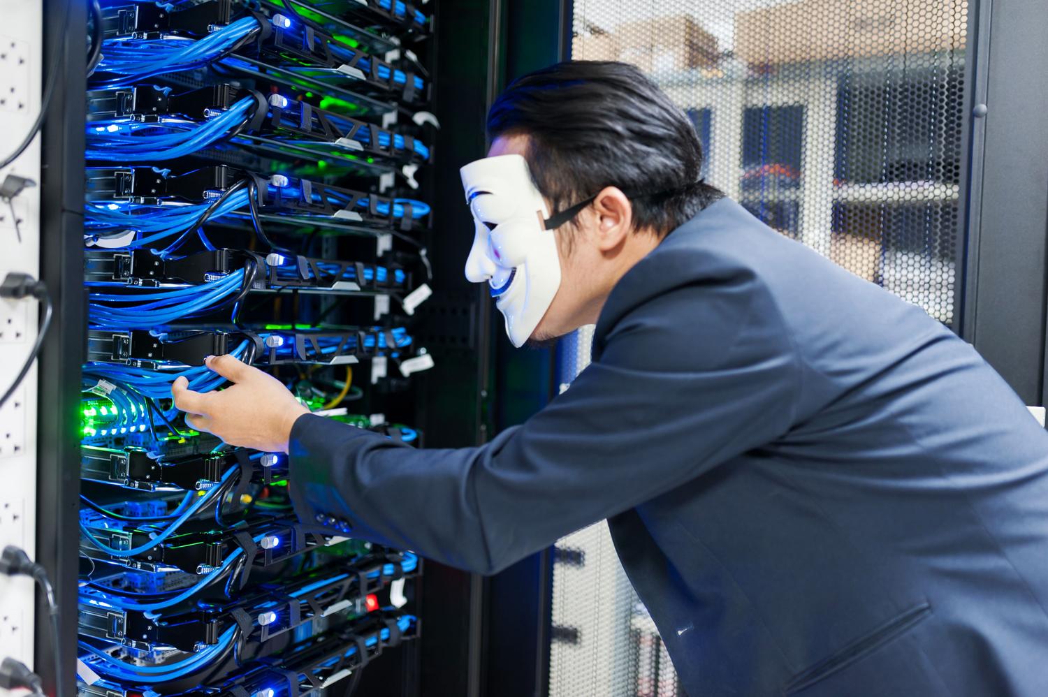 Persona enmascarada manipulando servidores, simbolizando las amenazas de ransomware y la necesidad de seguridad de datos.
