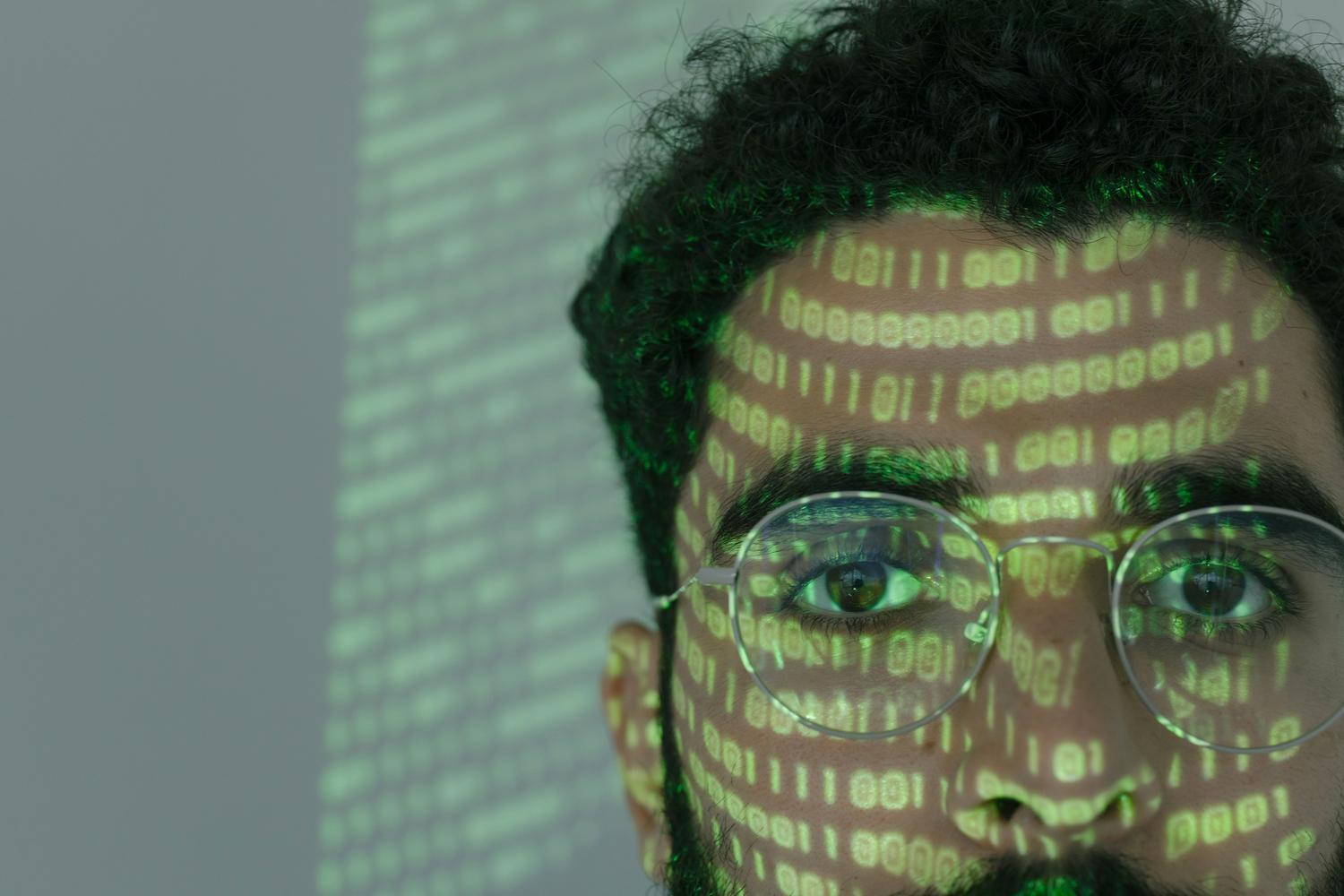 Primer plano de una persona con código binario proyectado en su rostro, simbolizando la ciberseguridad cognitiva.