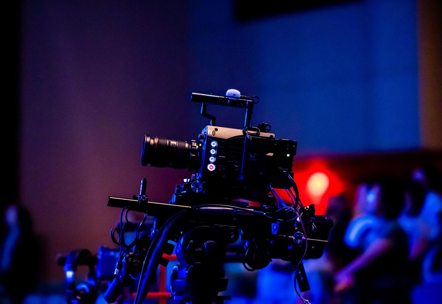 Cámara de broadcast profesional capturando la señal de un evento masivo con iluminación de escenario.