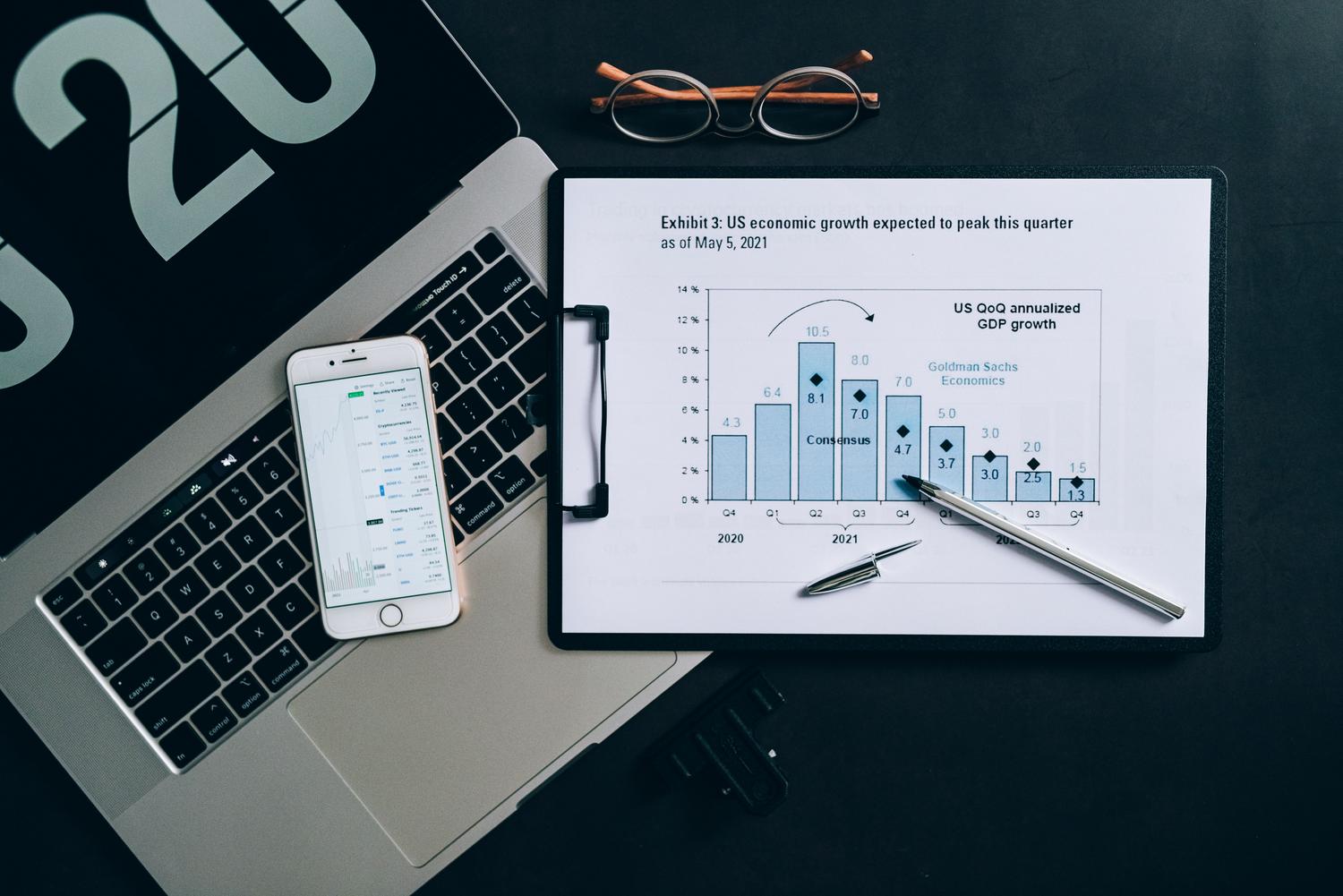 Espacio de trabajo moderno para análisis financiero con laptop, smartphone y reportes económicos impresos.