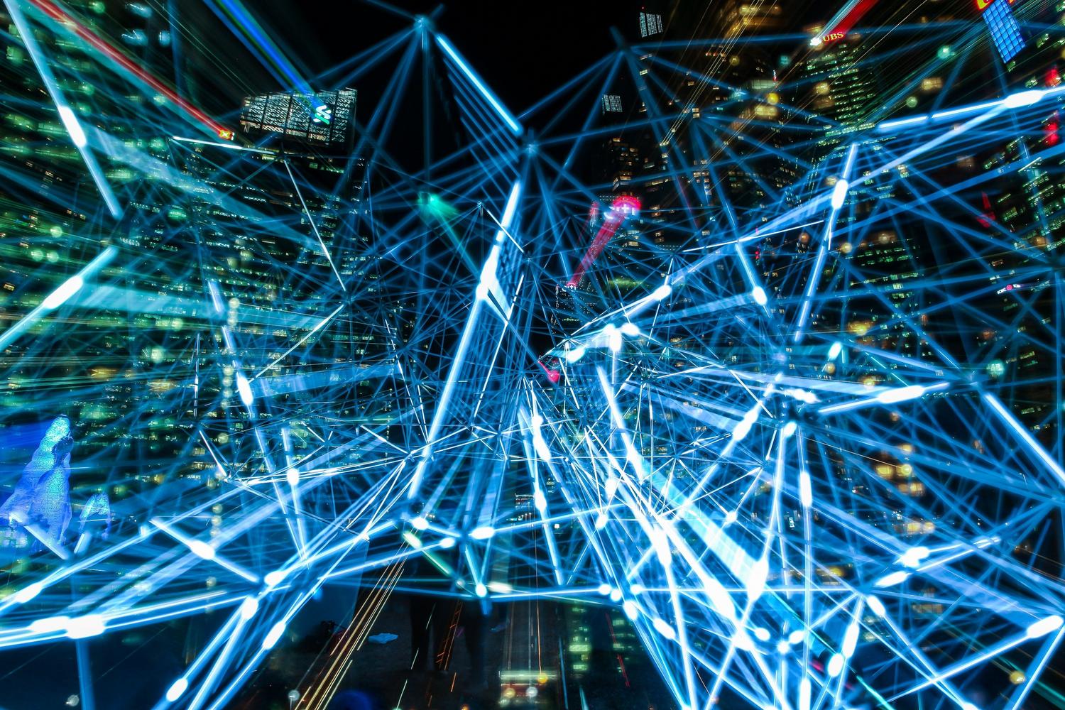 Trazos de luz azules interconectados sobre un paisaje urbano nocturno, representando la red digital y el flujo de información en un entorno empresarial.
