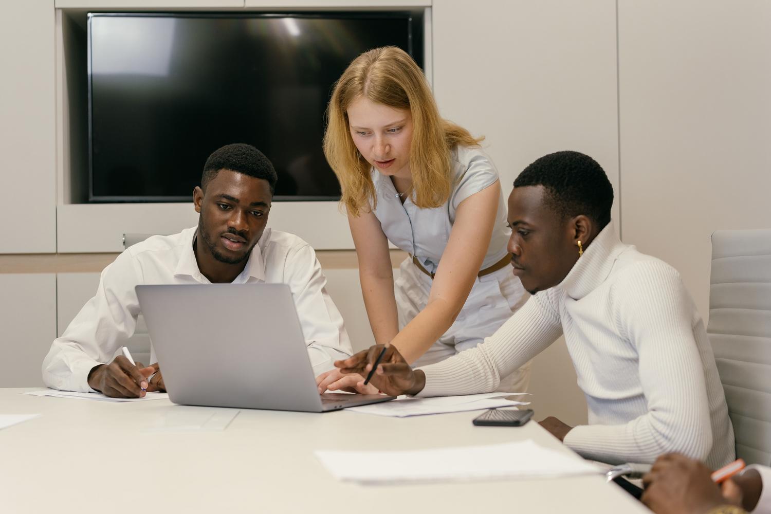Equipo de profesionales colaborando en una oficina moderna sobre un portátil, ilustrando la gestión del conocimiento y la productividad corporativa.