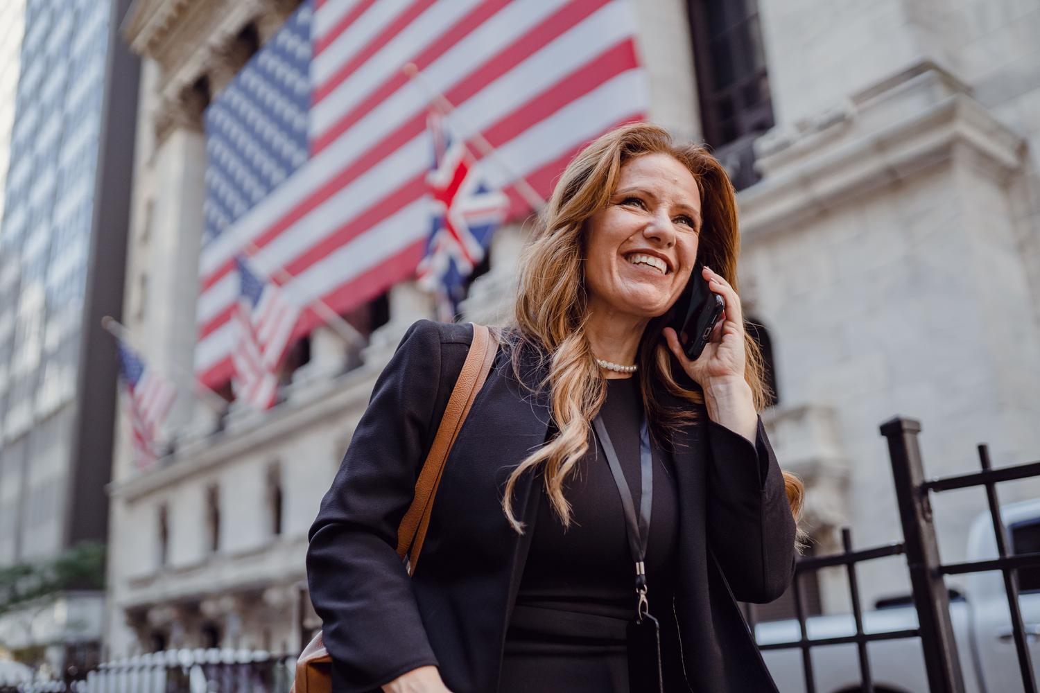 Mujer empresaria hablando por teléfono con banderas internacionales de fondo, representando el éxito en la comunicación en mercados occidentales.