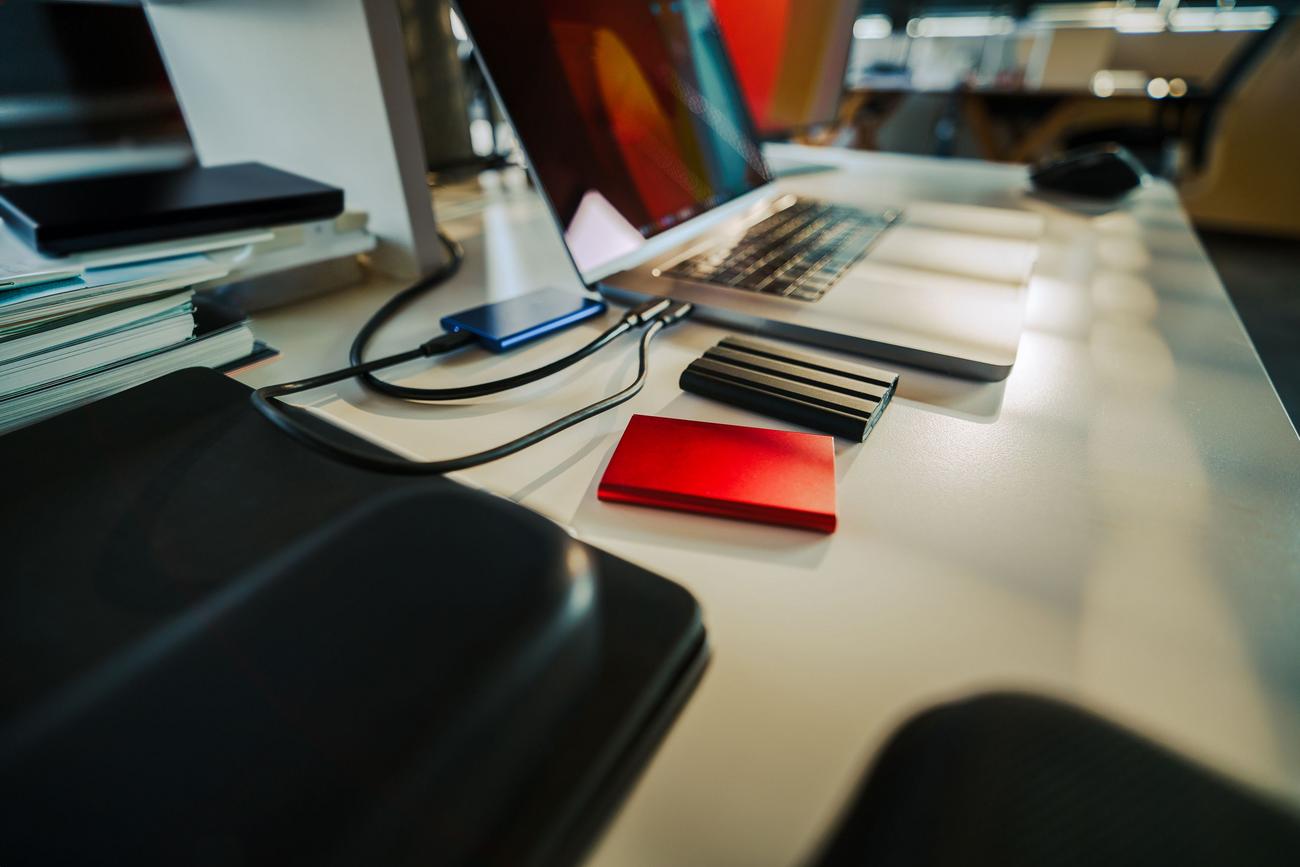 Escritorio de oficina organizado con diversos discos duros externos conectados a un portátil.