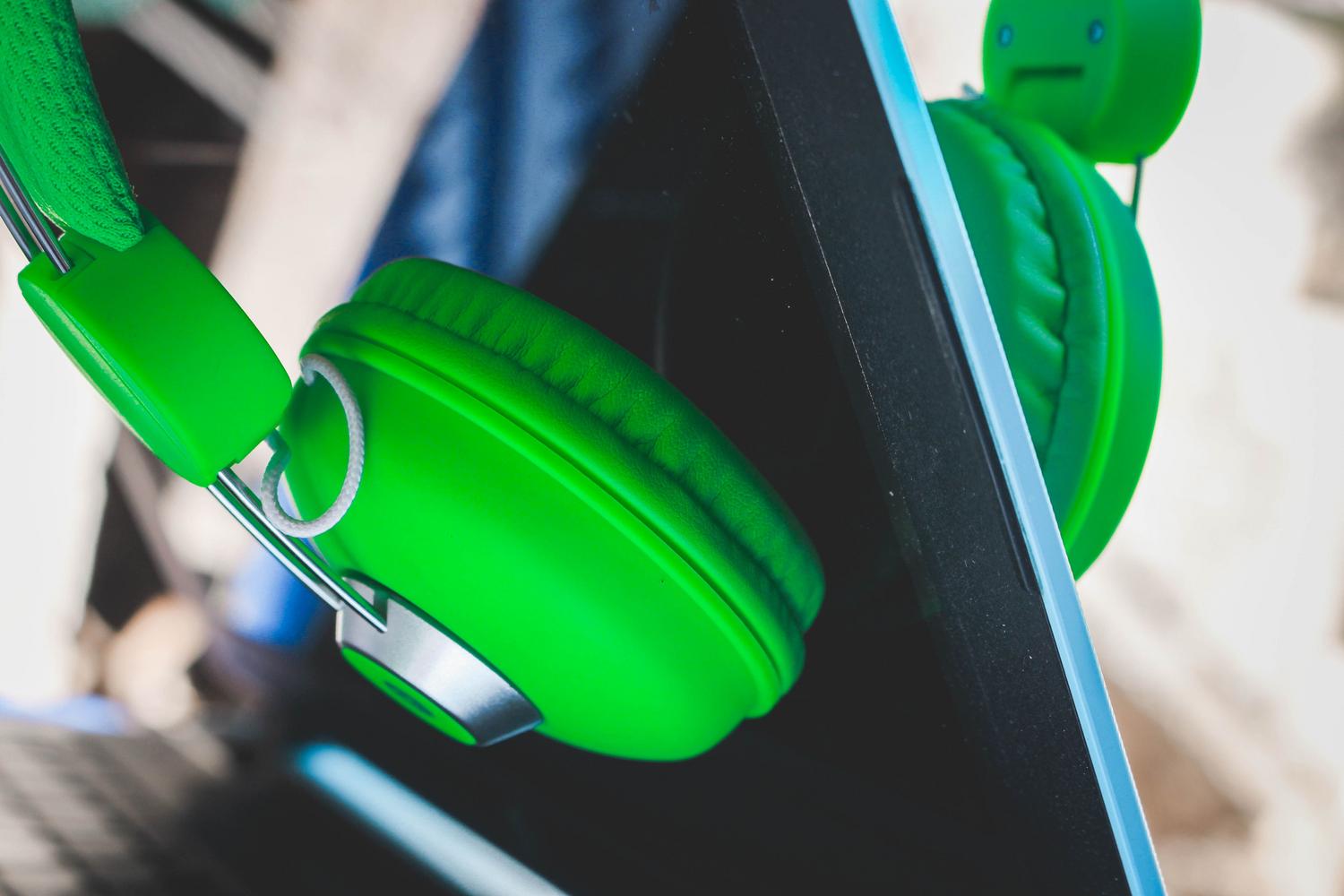 Auriculares de color verde vibrante apoyados en la pantalla de un portátil, destacando la compatibilidad de accesorios inalámbricos.