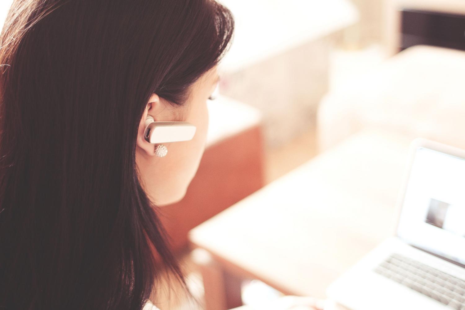 Mujer profesional utilizando un auricular Bluetooth mientras trabaja con su portátil en una oficina moderna.