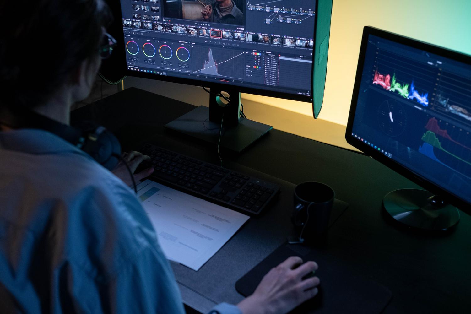 Editor de vídeo profesional trabajando con doble monitor en un estudio oscuro, enfatizando el enfoque y la estabilidad en la producción.