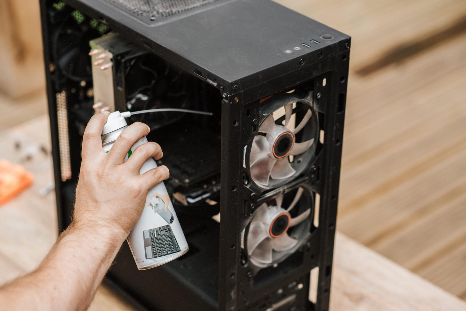 Persona limpiando el polvo de una unidad central de ordenador con aire comprimido para evitar el sobrecalentamiento de la GPU.