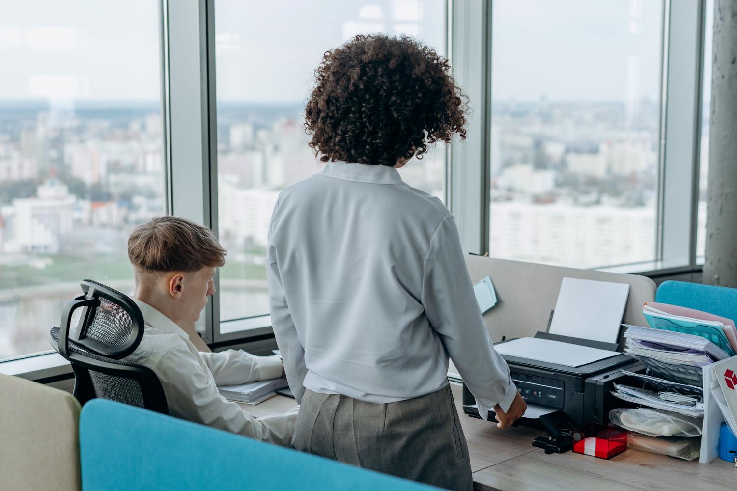 Empleados de oficina compartiendo una impresora de red en un espacio de trabajo colaborativo y luminoso.