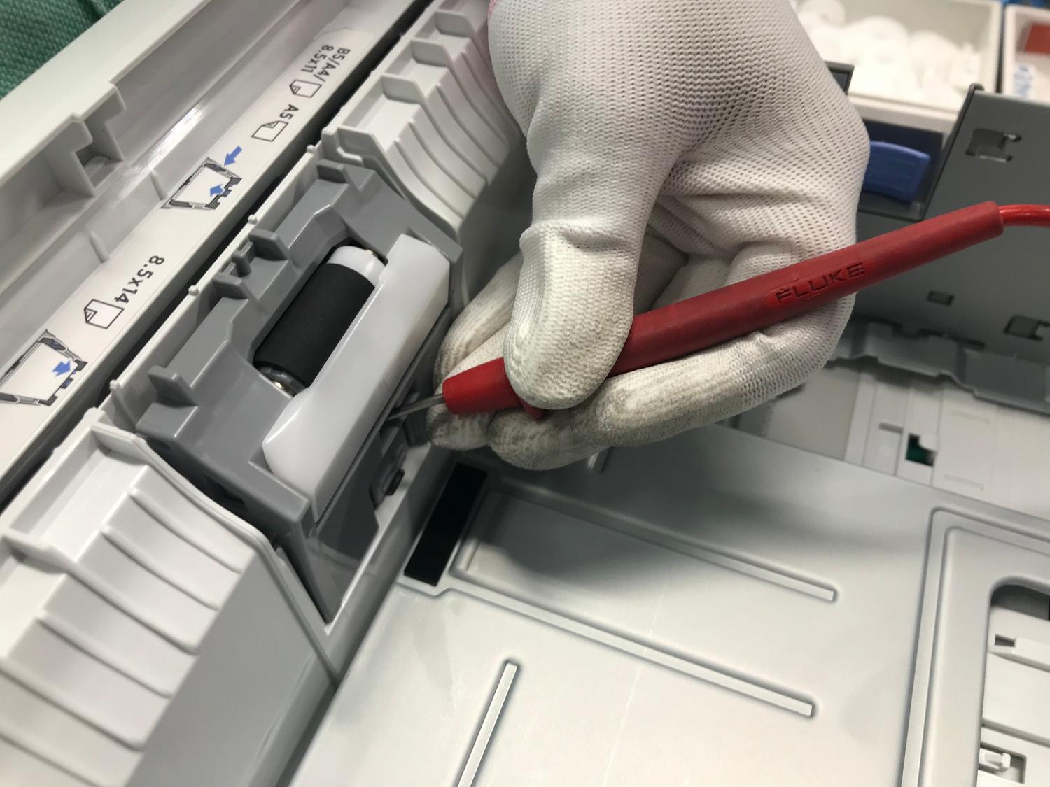 Primer plano de una mano enguantada reparando una impresora con una herramienta de precisión, representando el mantenimiento técnico