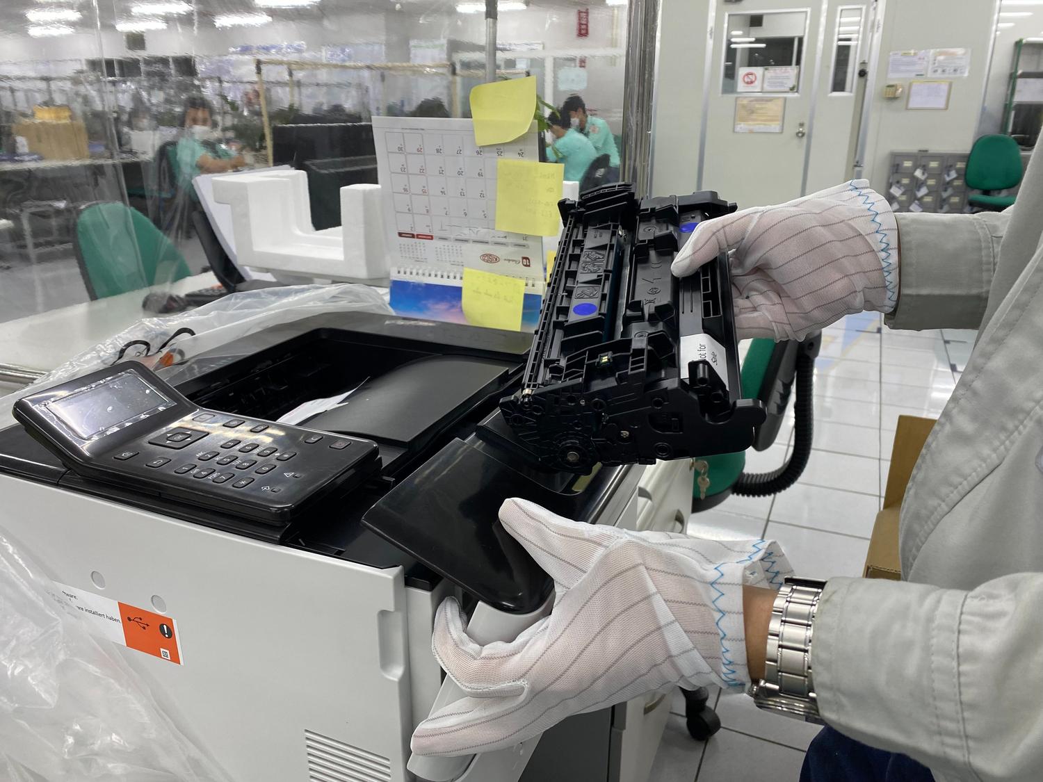 Operario sustituyendo un cartucho de tinta en una impresora, ideal para la sección de calidad de impresión y consumibles