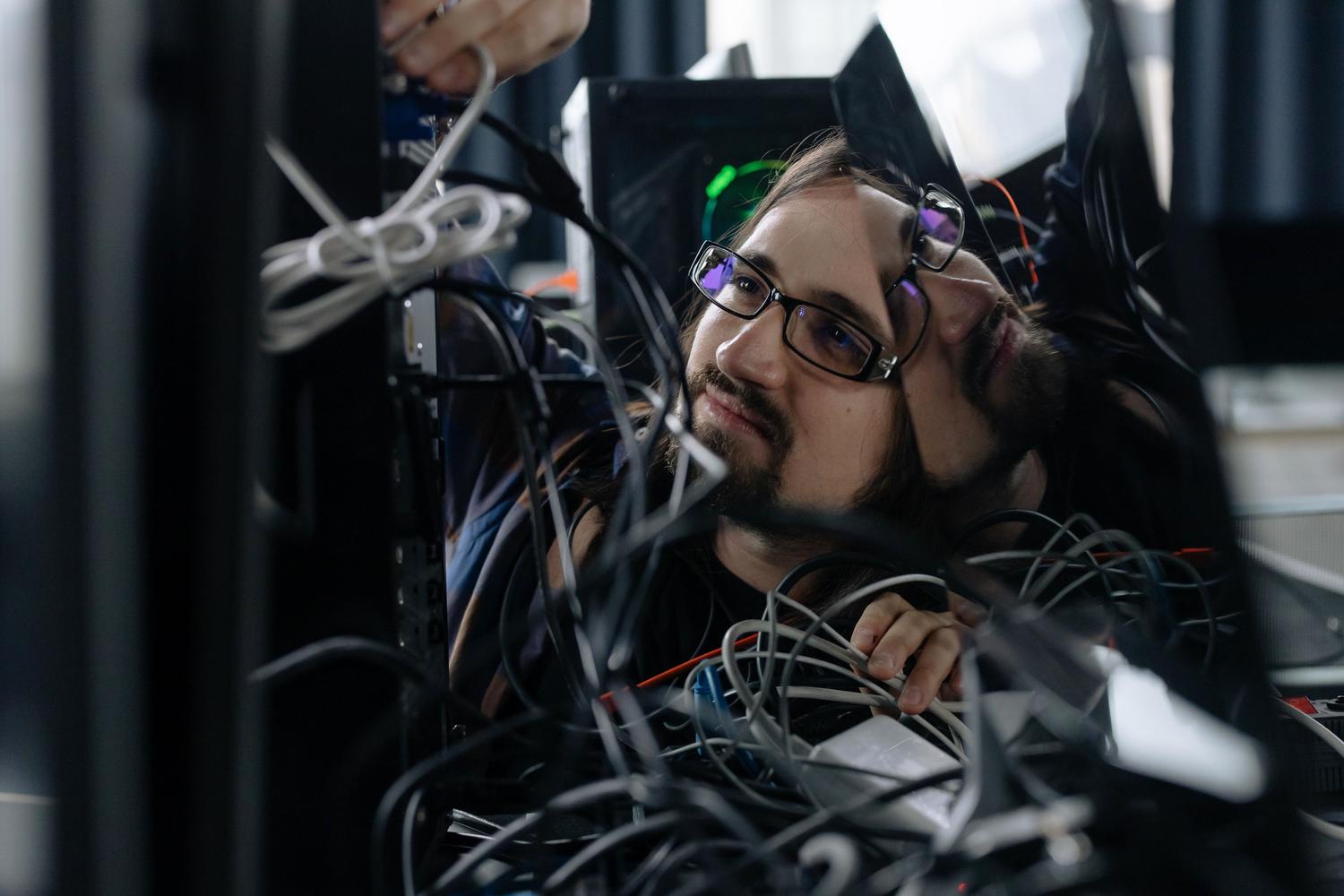 Técnico informático organizando cables enredados detrás de un ordenador, simbolizando la resolución de conflictos técnicos.