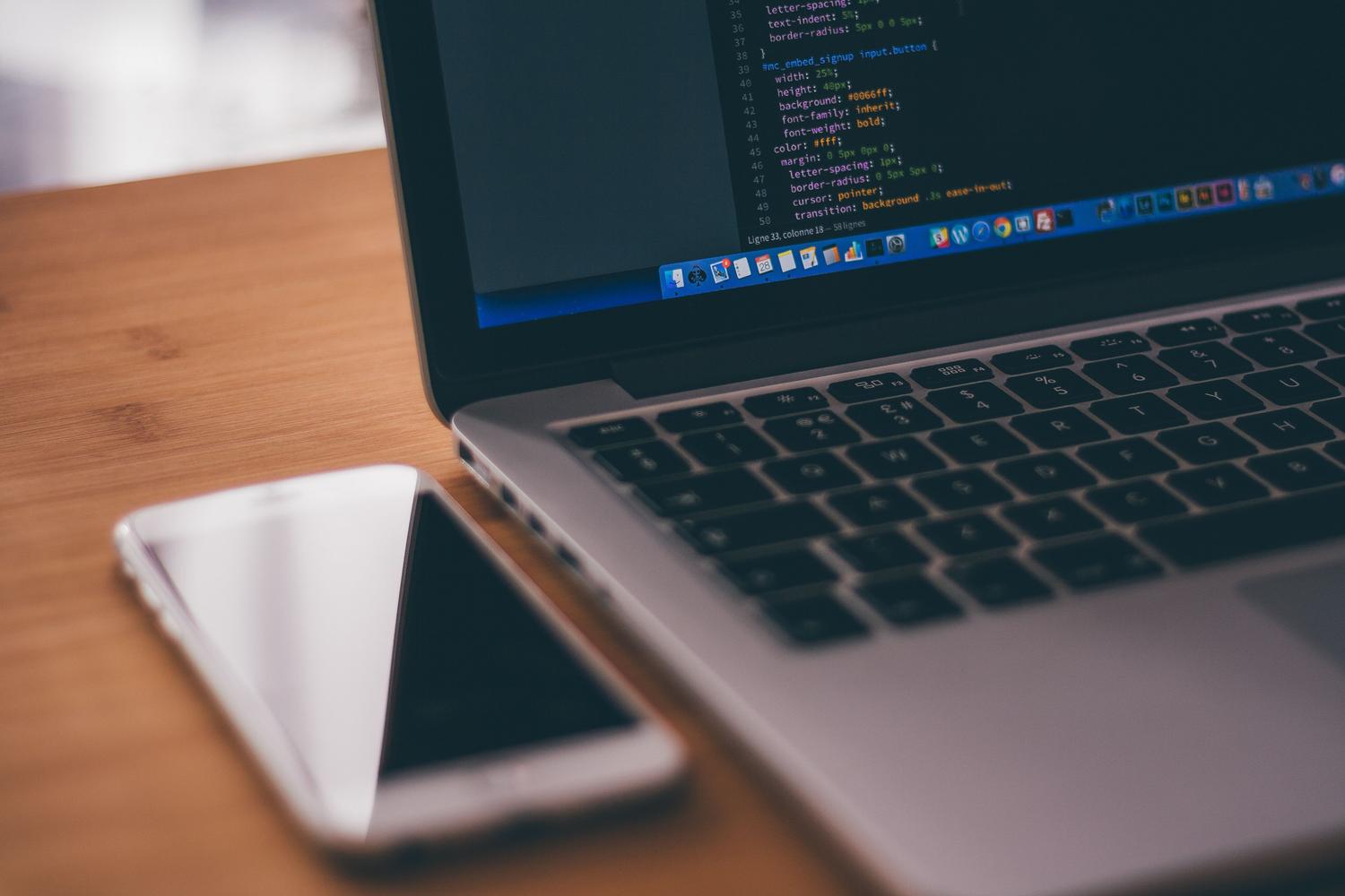 Entorno de desarrollo con un ordenador portátil mostrando código y un smartphone al lado, representando las pruebas de desarrollo y desarrollo de apps.