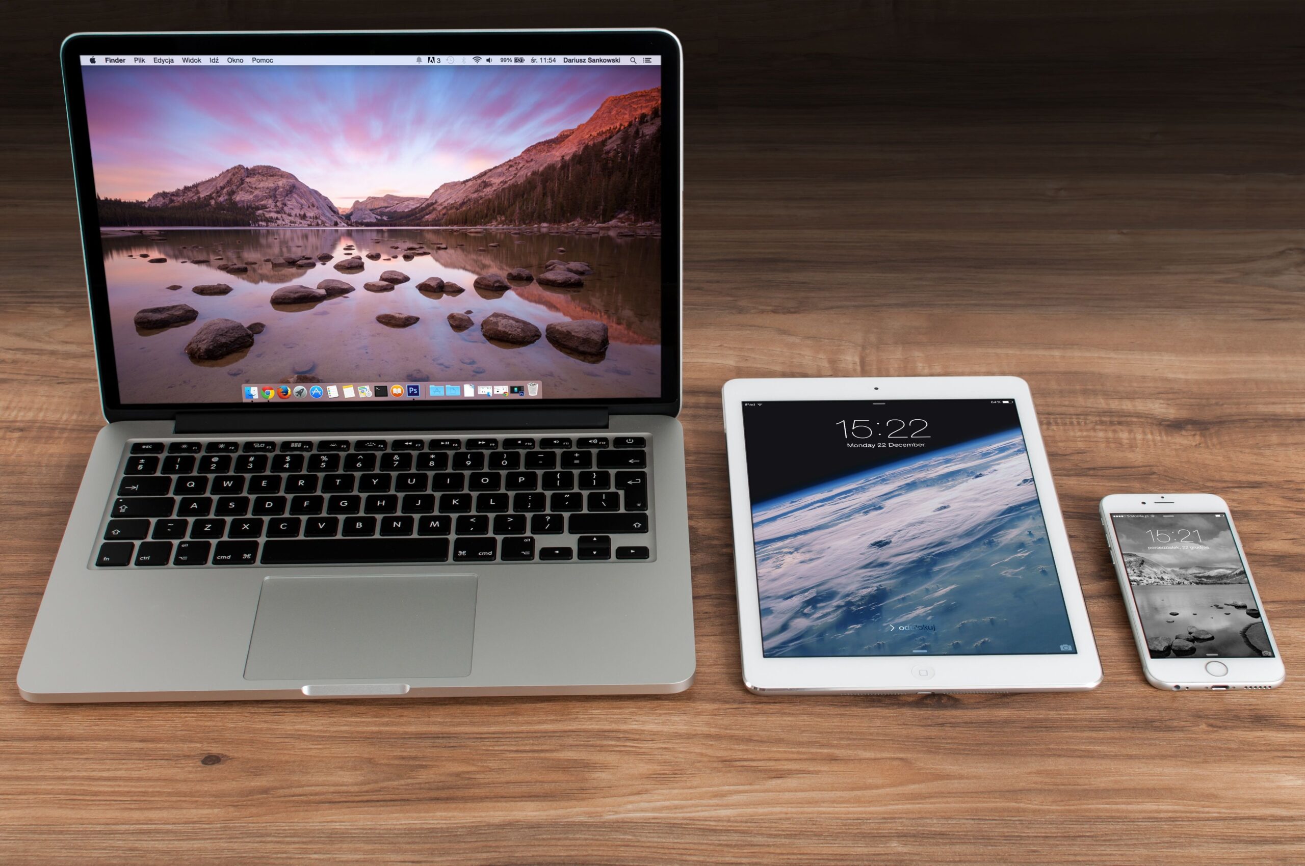 Ecosistema de dispositivos Apple (MacBook, iPad e iPhone) sincronizados sobre un escritorio de madera.