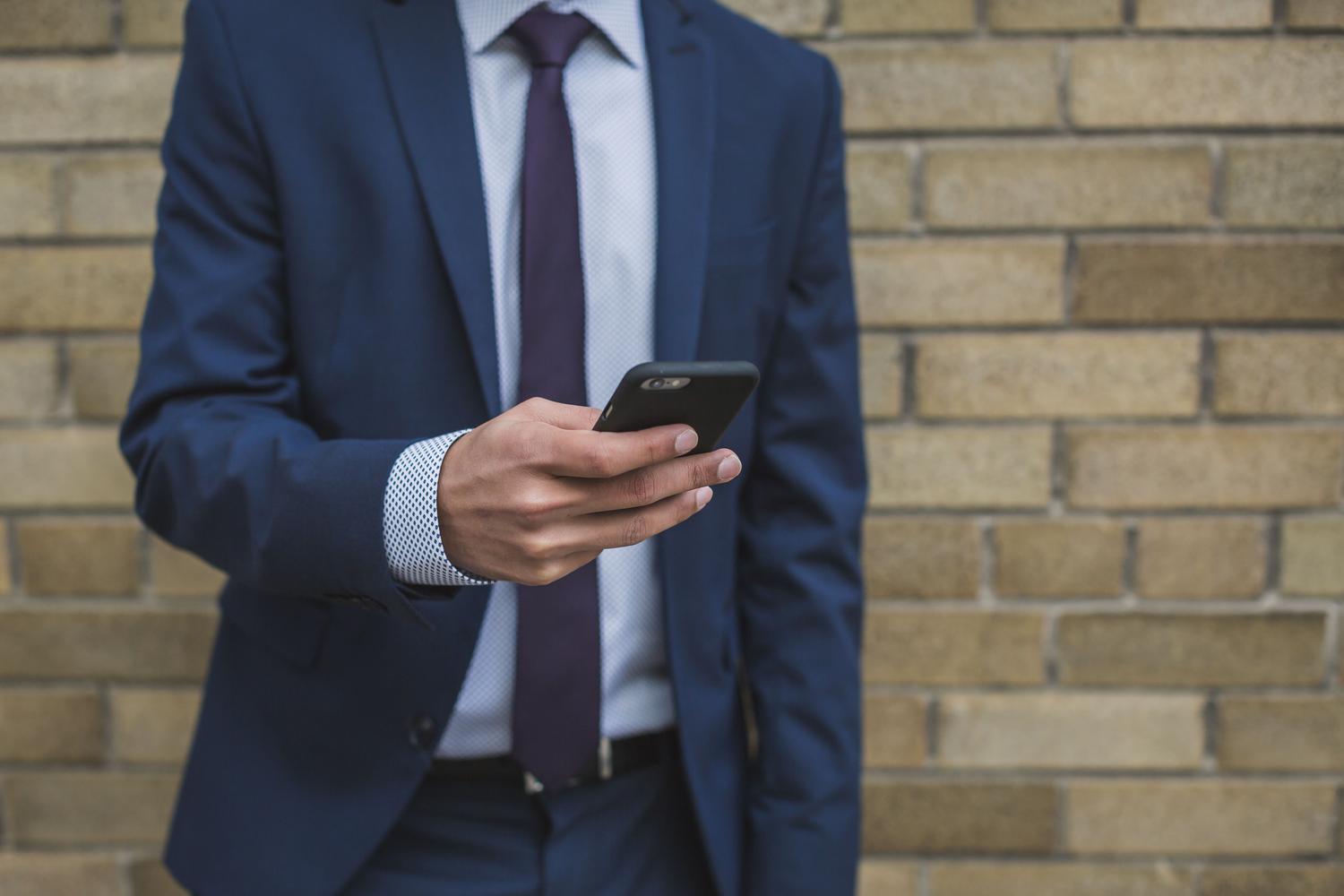 Ejecutivo B2B en traje utilizando su móvil, representando la interceptación quirúrgica del decisor correcto en redes sociales.