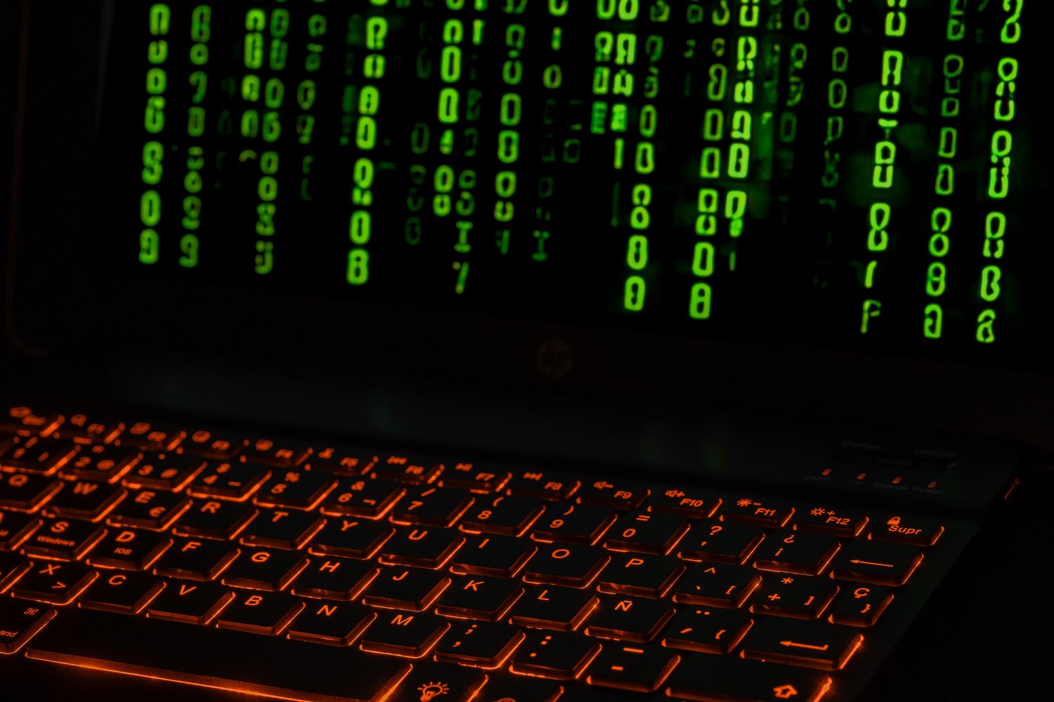 Teclado de ordenador con retroiluminación naranja y código digital verde en pantalla, ilustrando el concepto de firmware y software interno.
