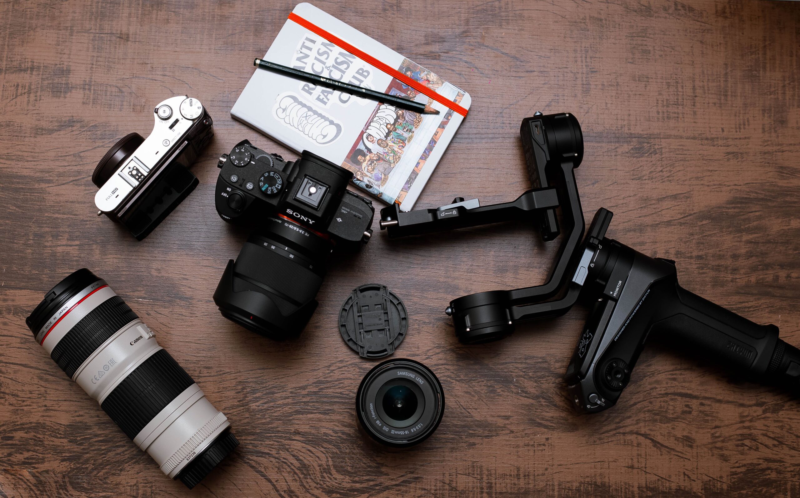 Plano cenital de equipo fotográfico con diversas lentes y un gimbal, ilustrando la necesidad de actualizar el firmware tanto de cuerpos como de ópticas.