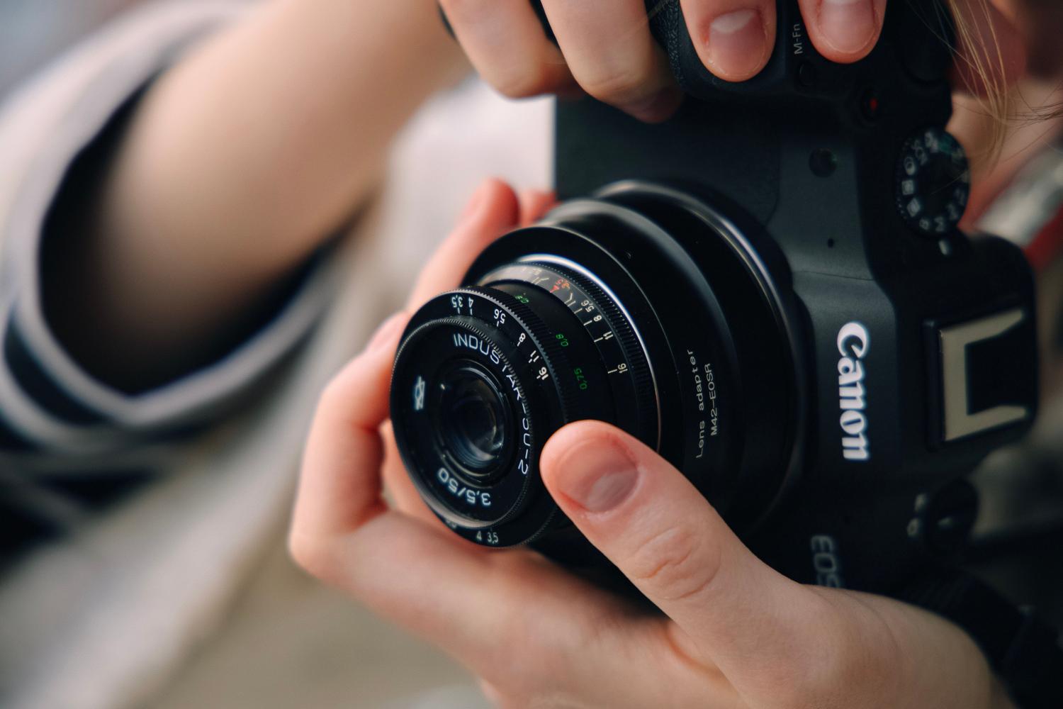 Primer plano de manos ajustando un objetivo vintage Industar-22 en una cámara Canon mirrorless moderna mediante un adaptador de montura.