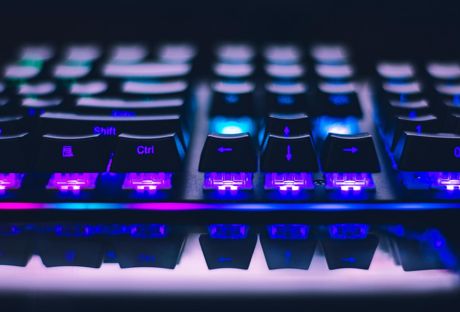 Detalle artístico de las teclas de un teclado mecánico con iluminación RGB en tonos azules y púrpuras, enfocándose en la calidad del hardware.