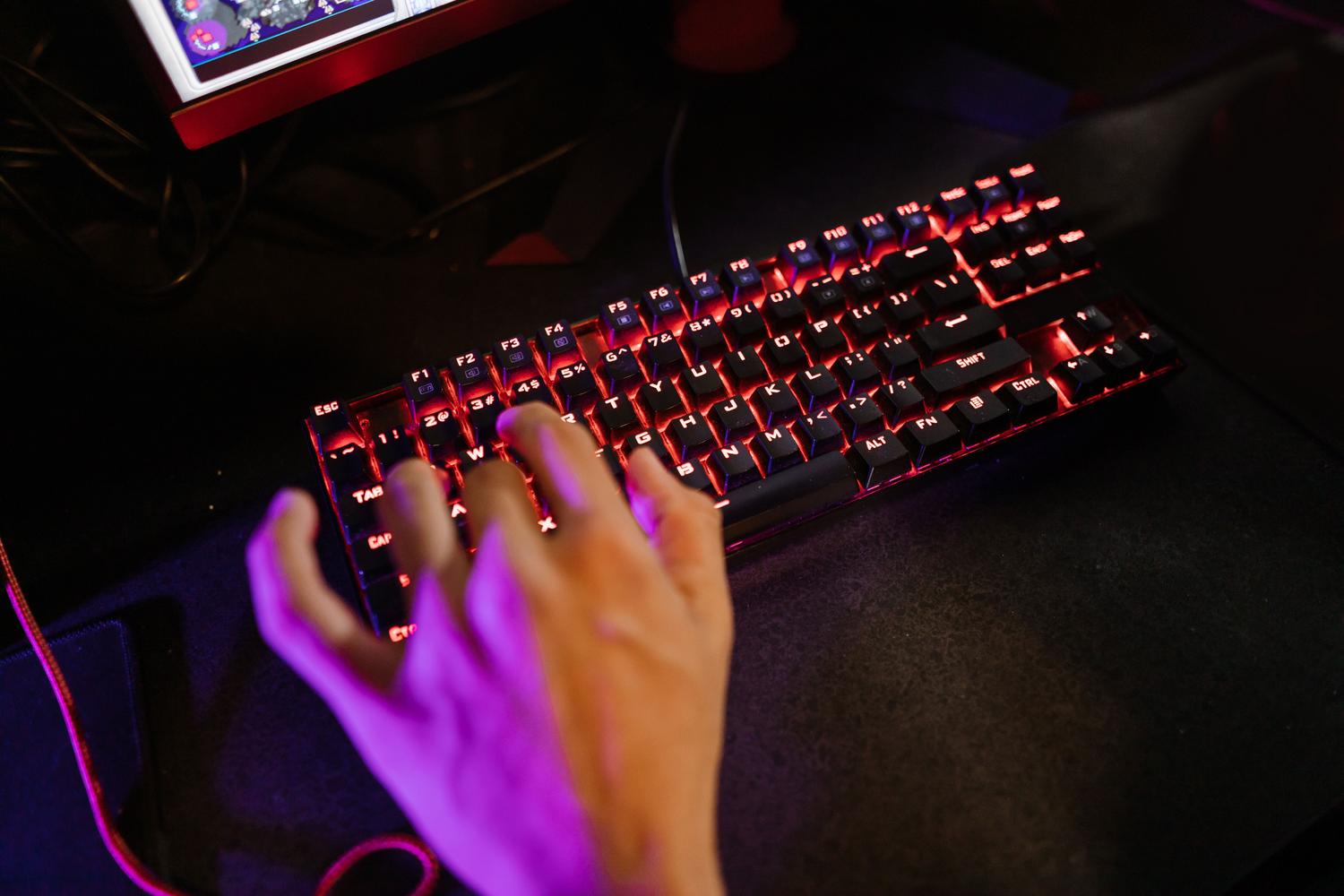 Primer plano de una persona utilizando un teclado mecánico con retroiluminación roja en un entorno oscuro, ideal para representar la acción de programar macros.