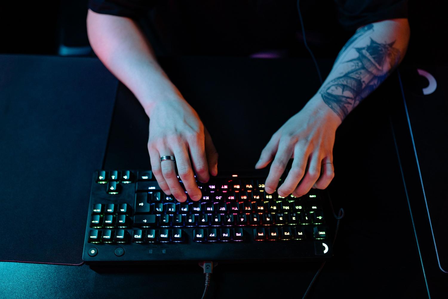 Persona escribiendo en un teclado mecánico RGB con colores degradados, evocando una atmósfera de gaming y alta productividad.