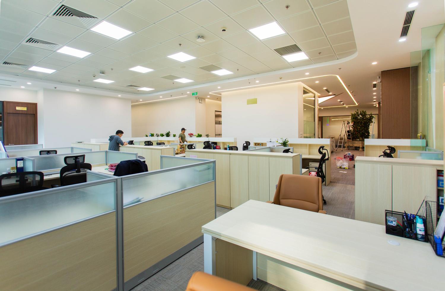 Interior de una oficina moderna, amplia y luminosa con cubículos abiertos, representando un entorno corporativo profesional.