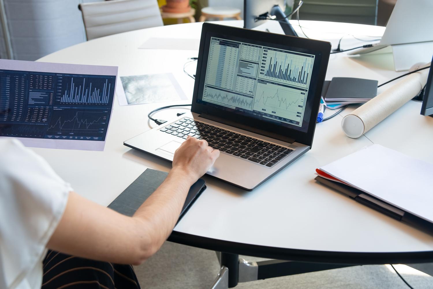 Profesional analizando gráficos de datos y tablas financieras en un portátil, representando el análisis de datos empresariales.