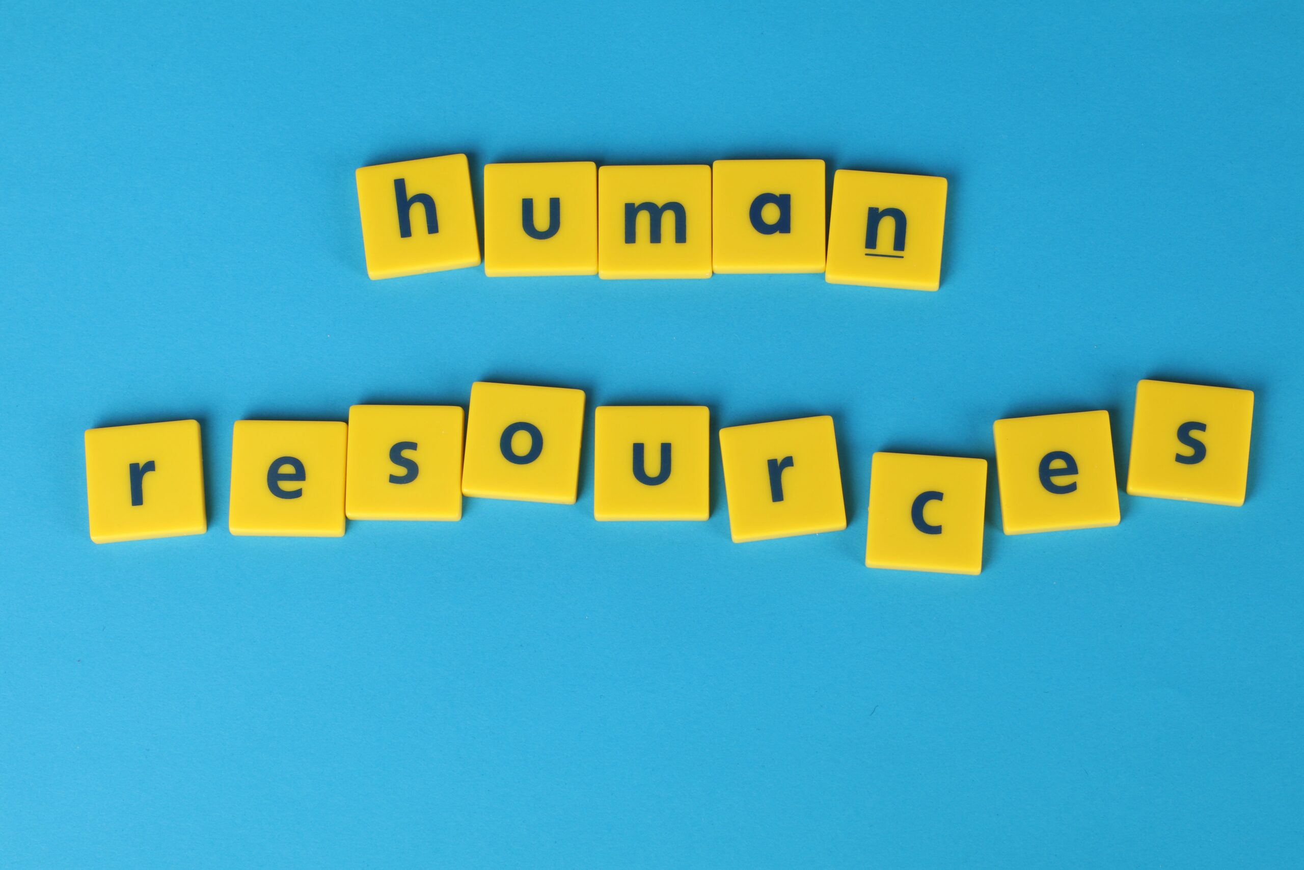 Fichas de madera que deletrean 'human resources' sobre un fondo azul, proporcionando un contexto general y claro sobre la gestión de capital humano.