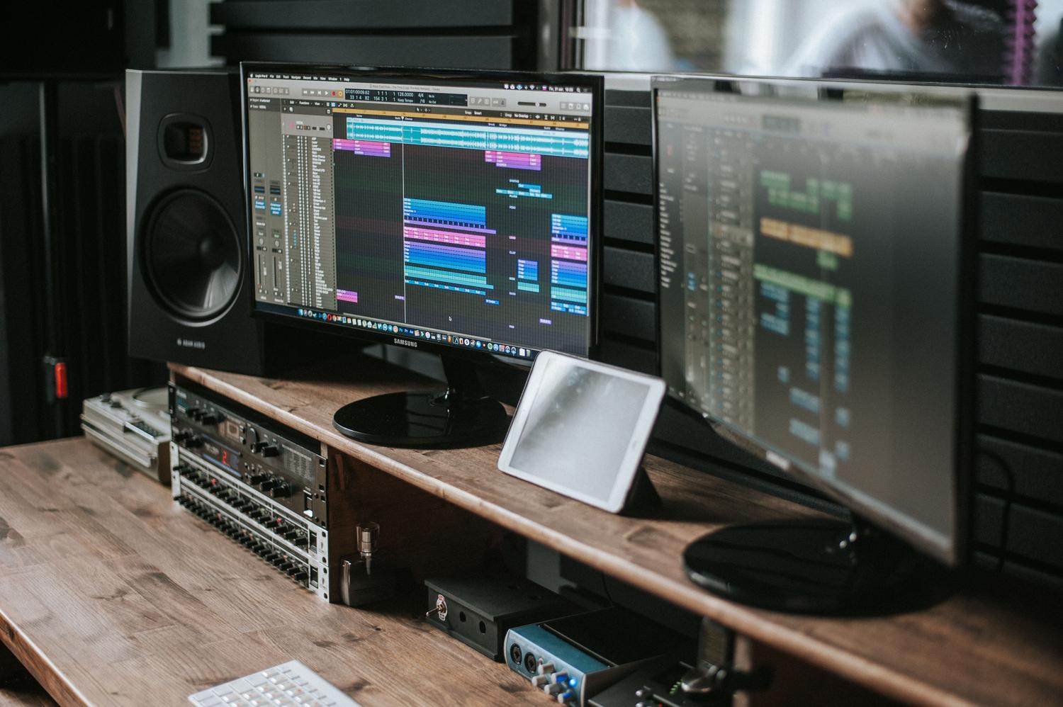 Estudio de música moderno con doble monitor mostrando software de edición de audio, ideal para ilustrar el flujo de trabajo profesional con IA.