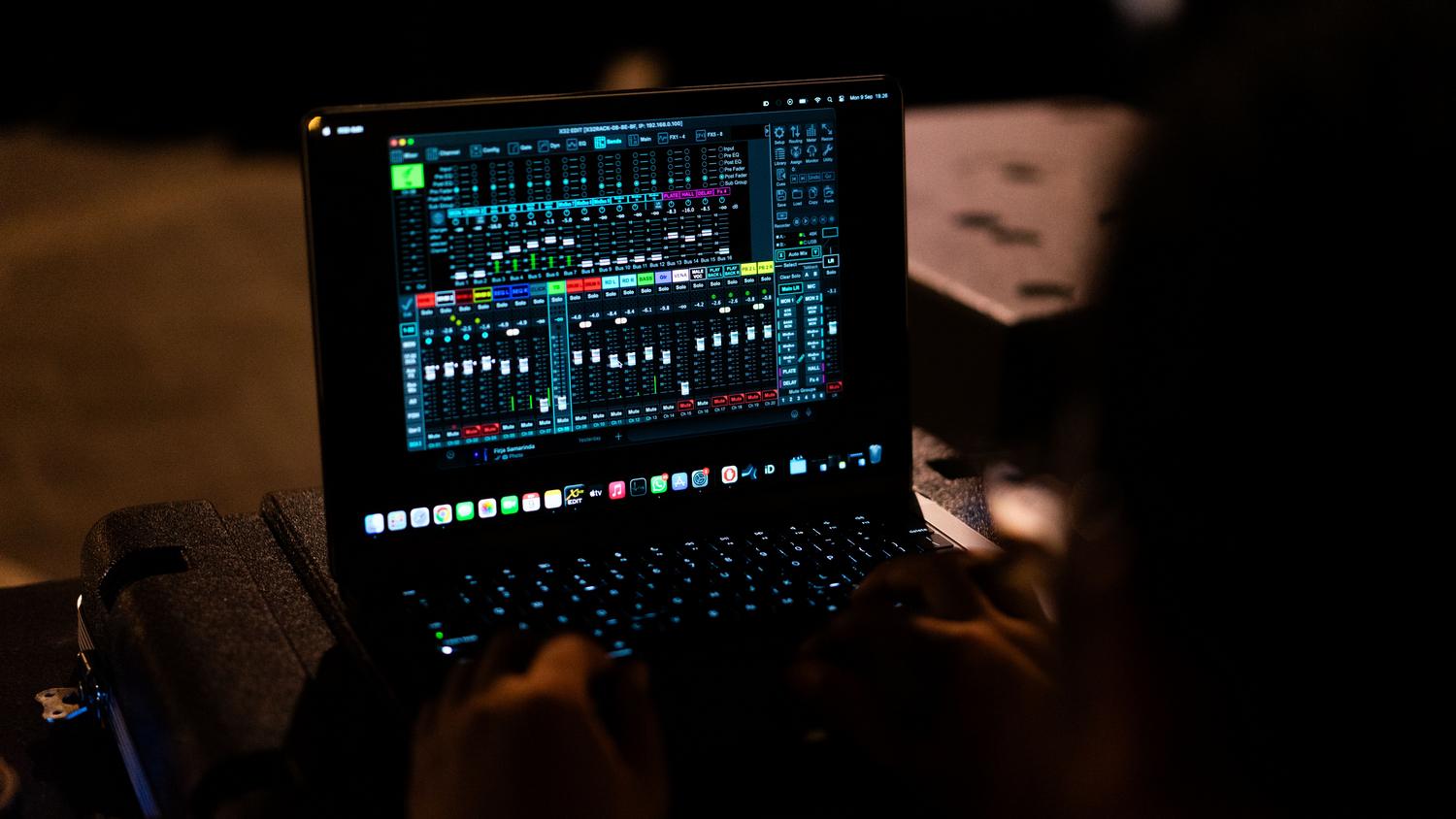 Ingeniero de sonido ajustando la configuración de audio en un mezclador digital a través de un portátil.