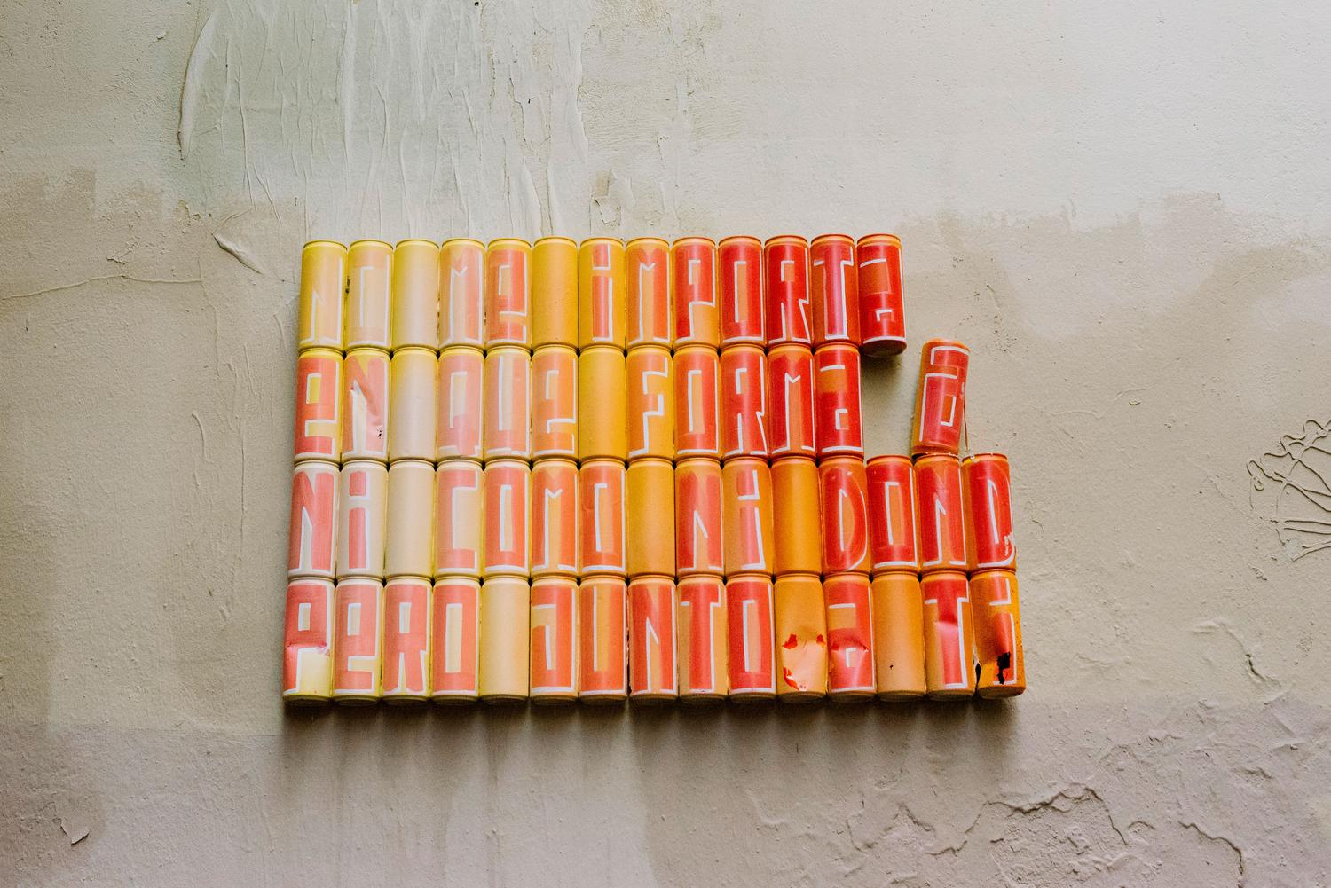 Instalación de arte urbano disruptiva utilizando latas de spray reales para formar un mensaje, ejemplificando la publicidad creativa que rompe la monotonía.