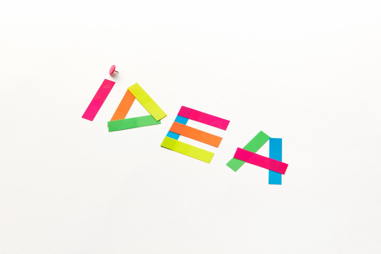 Composición creativa de la palabra IDEA formada con cintas de colores sobre fondo blanco, simbolizando la fase de brainstorming y conceptualización publicitaria.