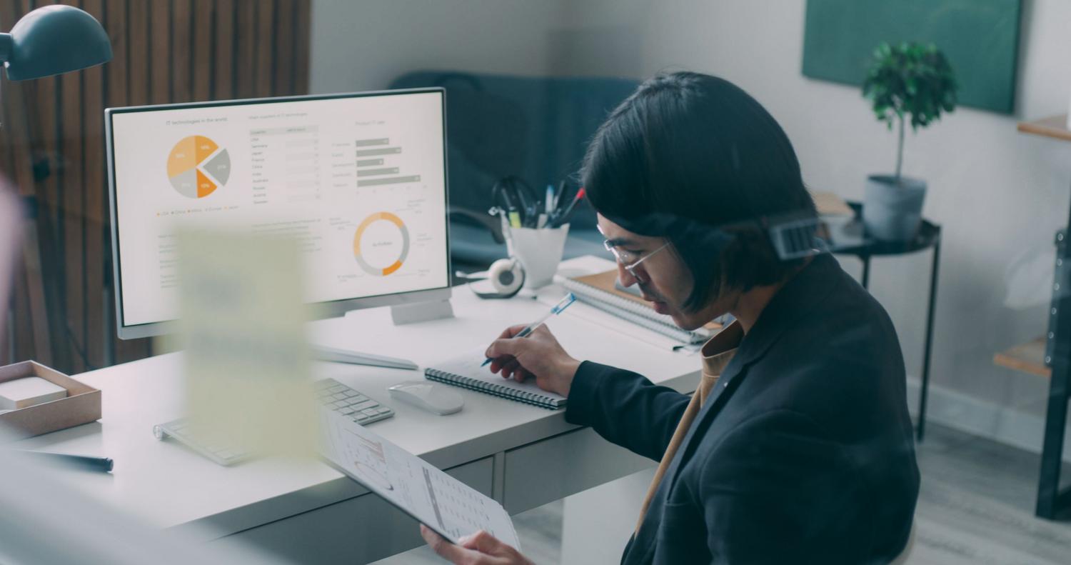 Profesional revisando un resumen ejecutivo impreso y comparándolo con un dashboard de datos en pantalla, representando la síntesis de información de alto nivel.