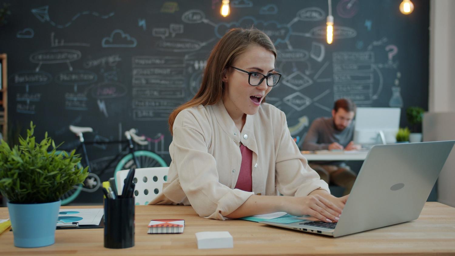 Mujer profesional sorprendida y satisfecha frente a su portátil en una oficina moderna, ilustrando la eficiencia y el impacto de un prompt de IA bien diseñado.