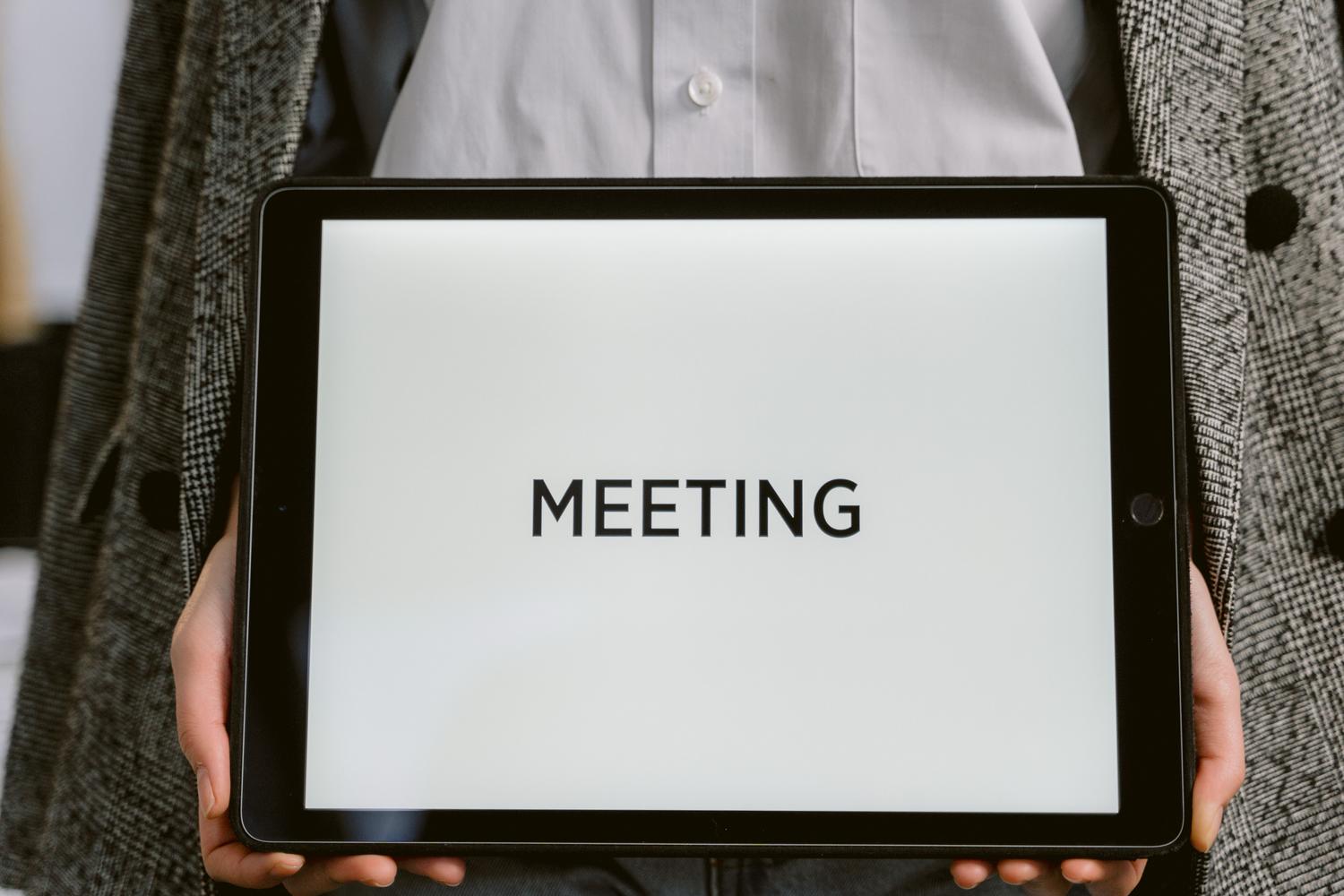 Primer plano de una tablet digital con el texto MEETING indicando el inicio de una reunión