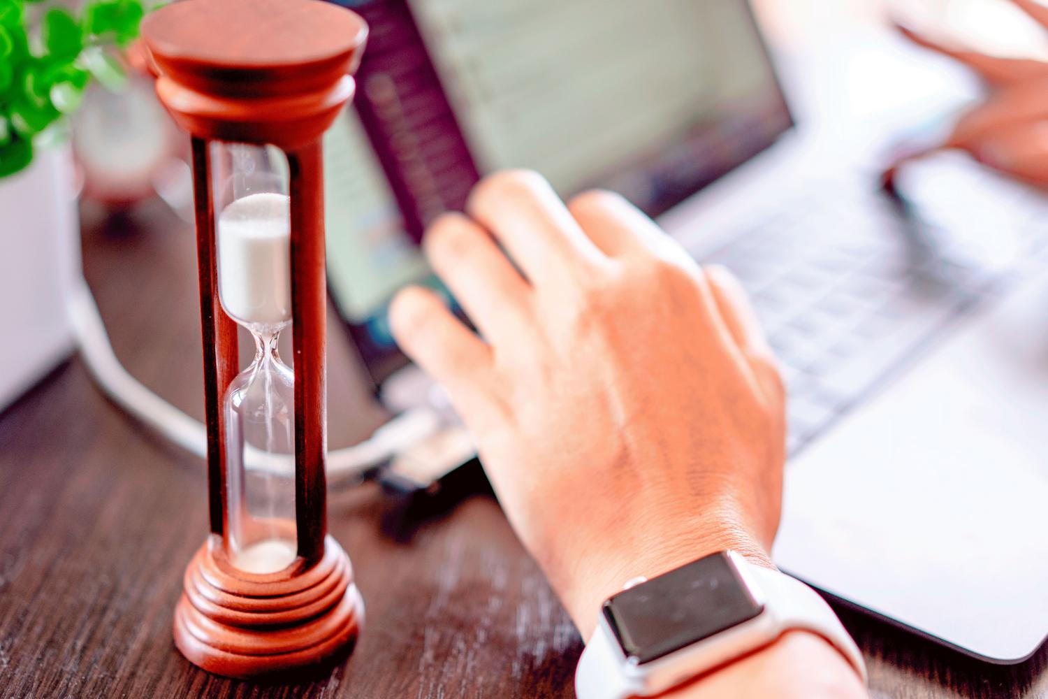 Reloj de arena sobre un ordenador portátil simbolizando la gestión del tiempo y la productividad