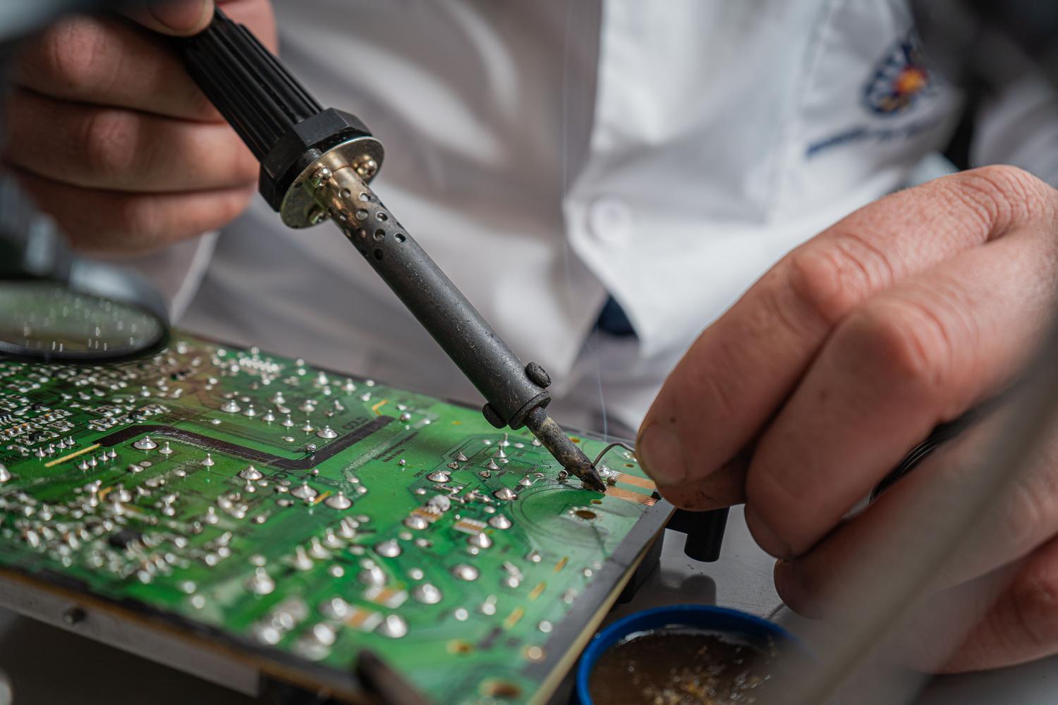 Técnico realizando un proceso de soldadura de precisión en una placa de circuito electrónico para la reparación de componentes.